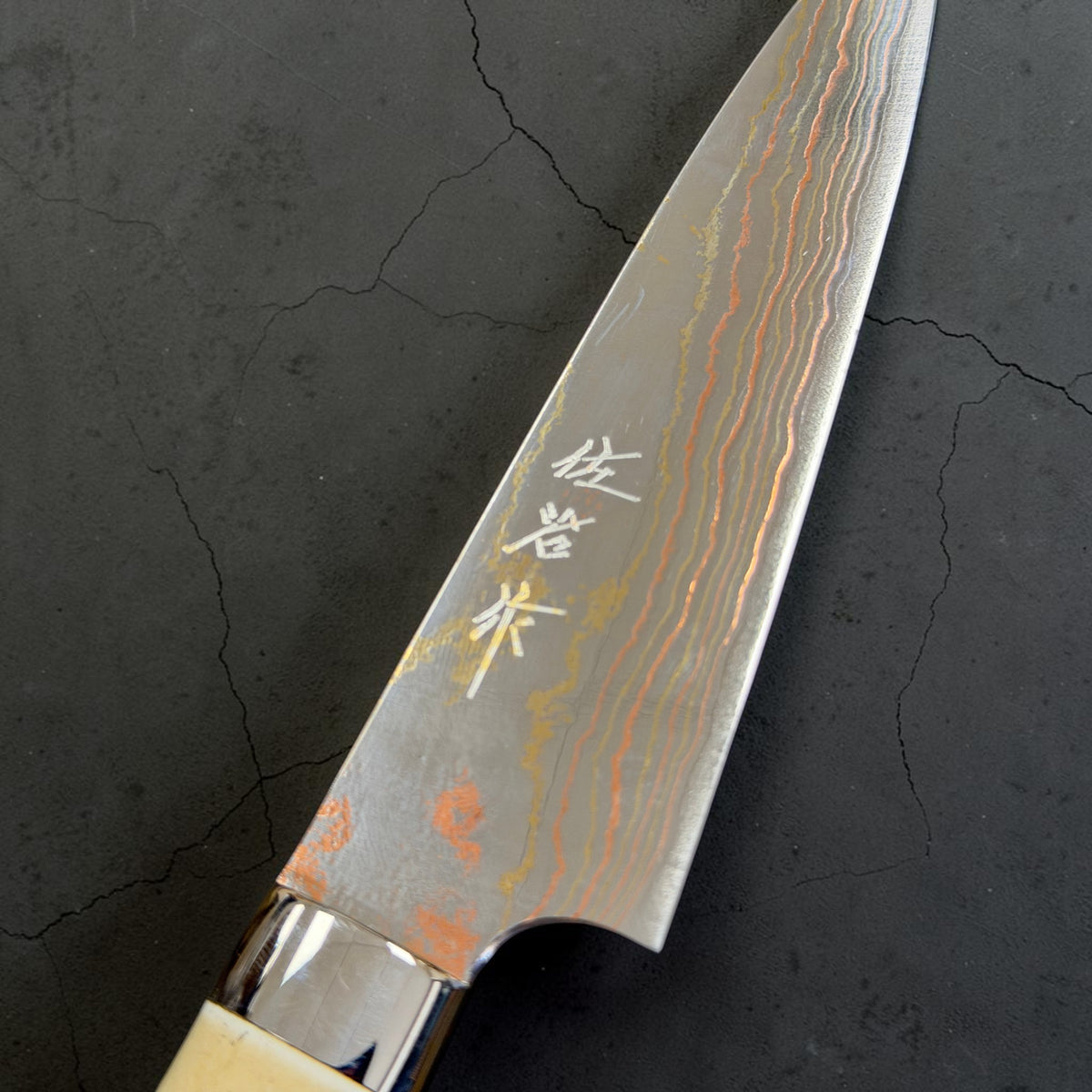 Kanji and rainbow detail of Takeshi Saji Blue #2 Rainbow Damascus Petty 130mm with white cow-horn western handle.