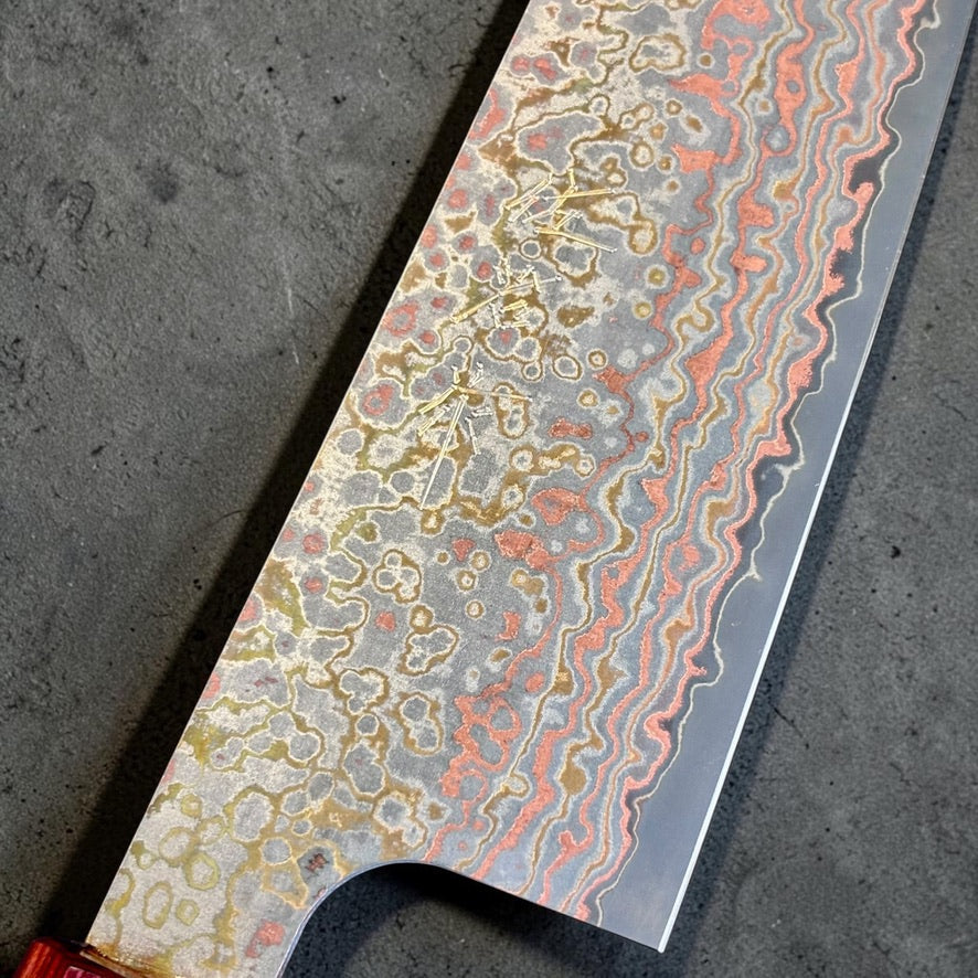 Close-up of Takeshi Saji maker marks and the copper, brass, and stainless Rainbow Damascus cladding on the VG-10W Gyuto.