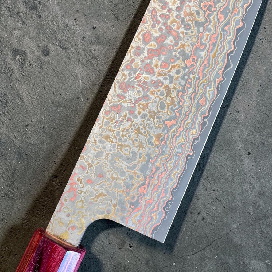 Close-up of the Takeshi Saji VG-10W Nashiji Rainbow Gyuto blade, maker marks, rainbow Damascus cladding, and red ferrule.