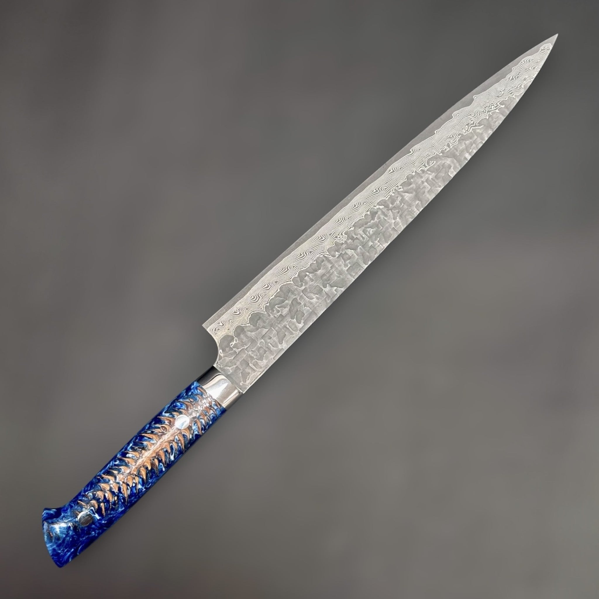 Takeshi Saji VG-10 Kuro Cross Tsuchime Sujihiki 240 mm with pinecone resin western handle, close angled view highlighting the cross tsuchime finish and layered VG-10 Damascus pattern.