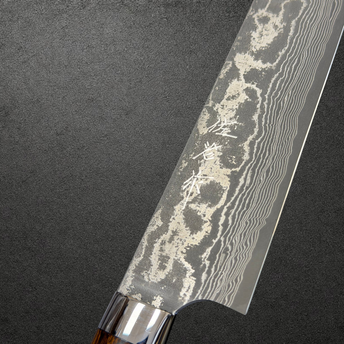Close-up of Takeshi Saji kanji and Kurozome Damascus layers above the polished bolster