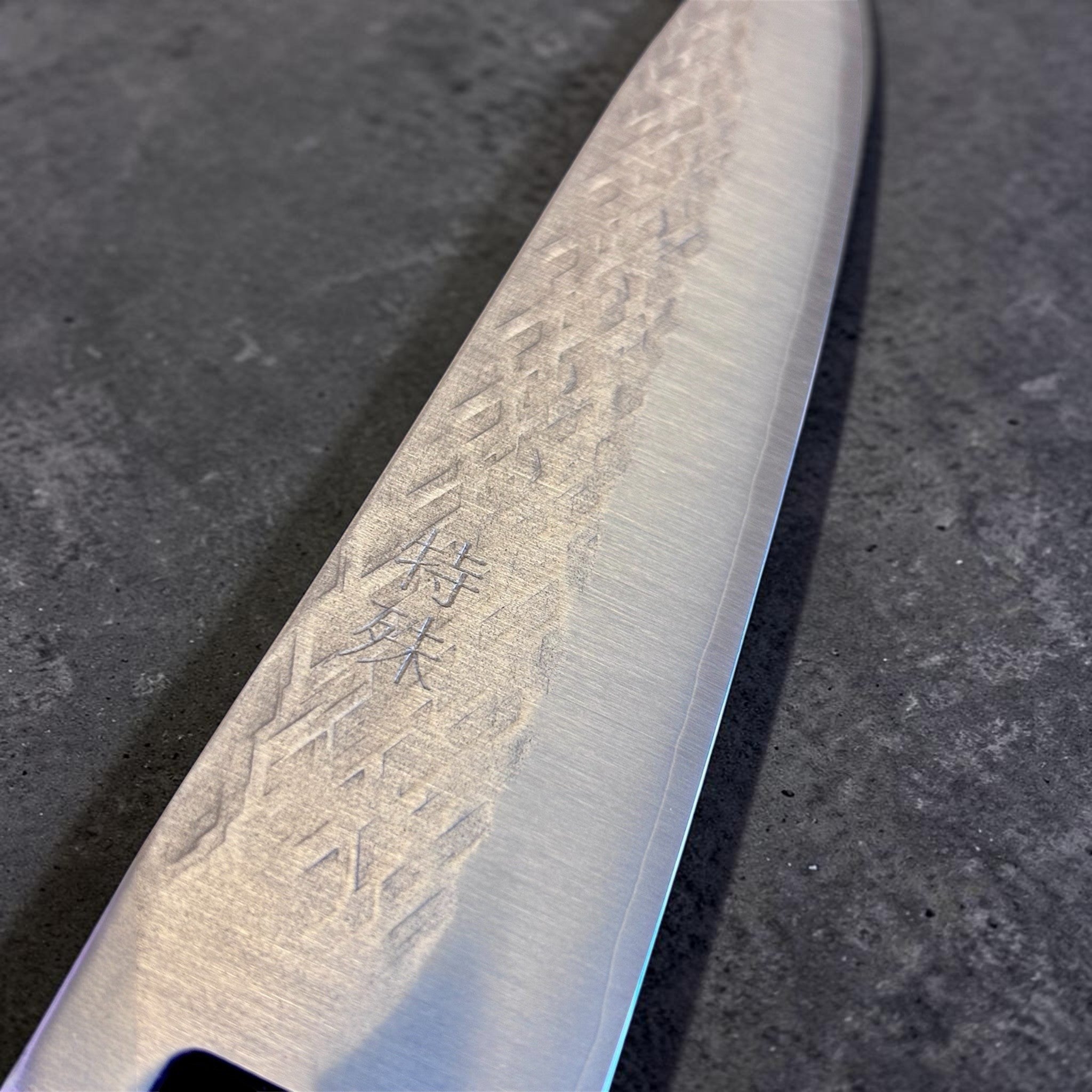 Tokushu Knife Tsuchime SLD Gyuto 210 mm, close-up detail of the blade face with engraved kanji and hammered tsuchime pattern.