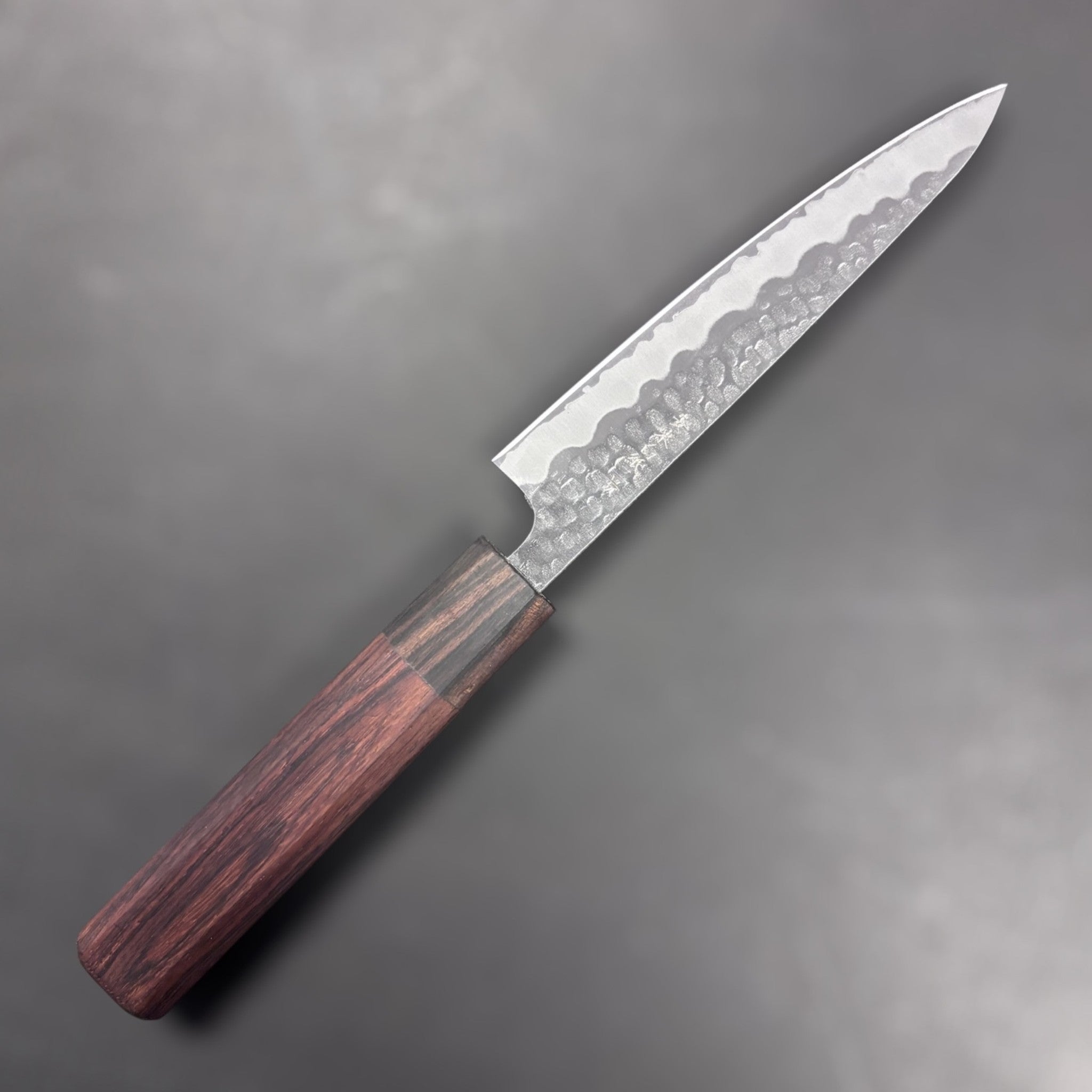 Tokushu Tsuchime White #2 Petty 135 mm with rosewood wa handle, front-left side profile of blade showing hammered cladding