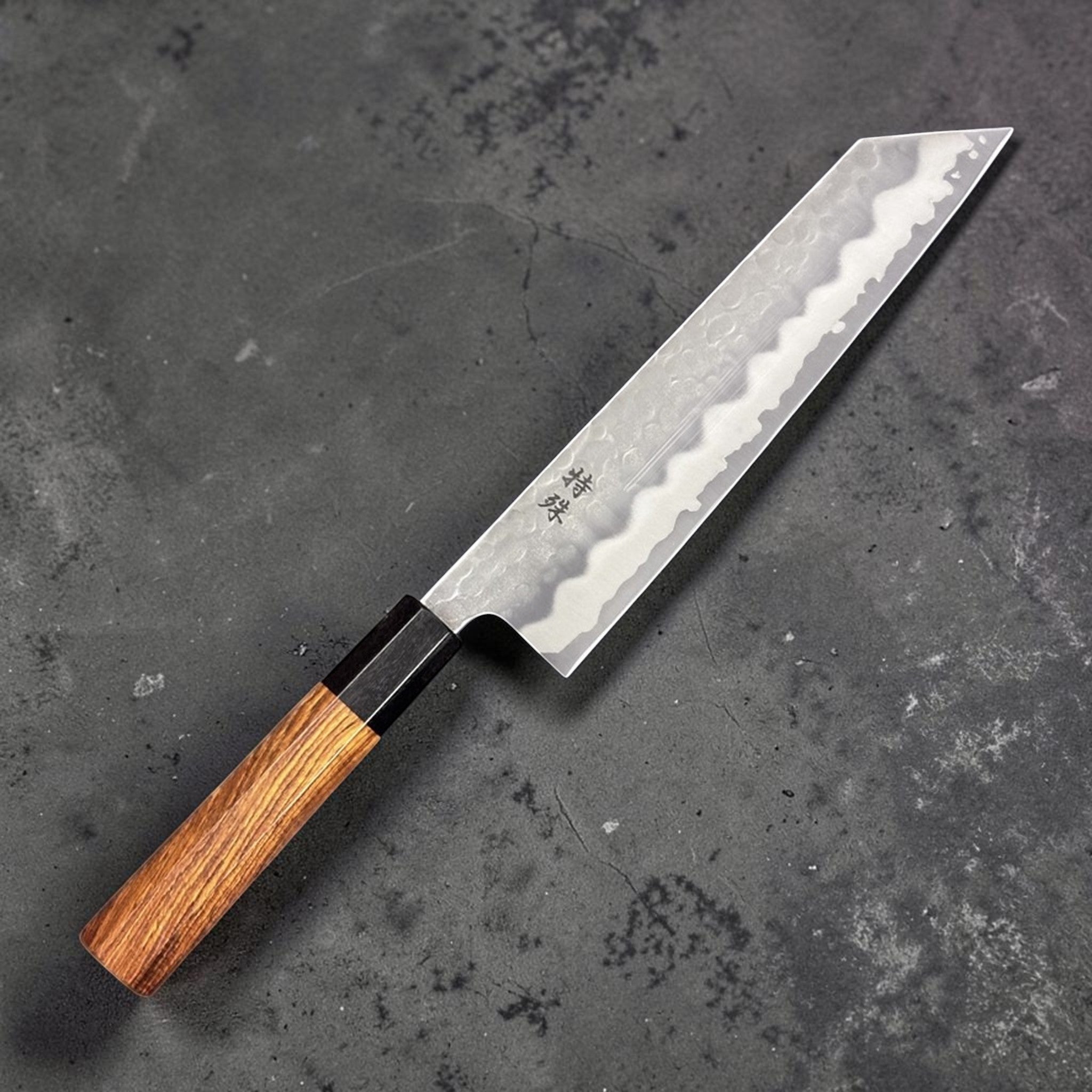 Tokushu White #2 Stainless Clad Tsuchime Kiritsuke 210mm, angled hero shot highlighting the tip and wa handle on a grey background.