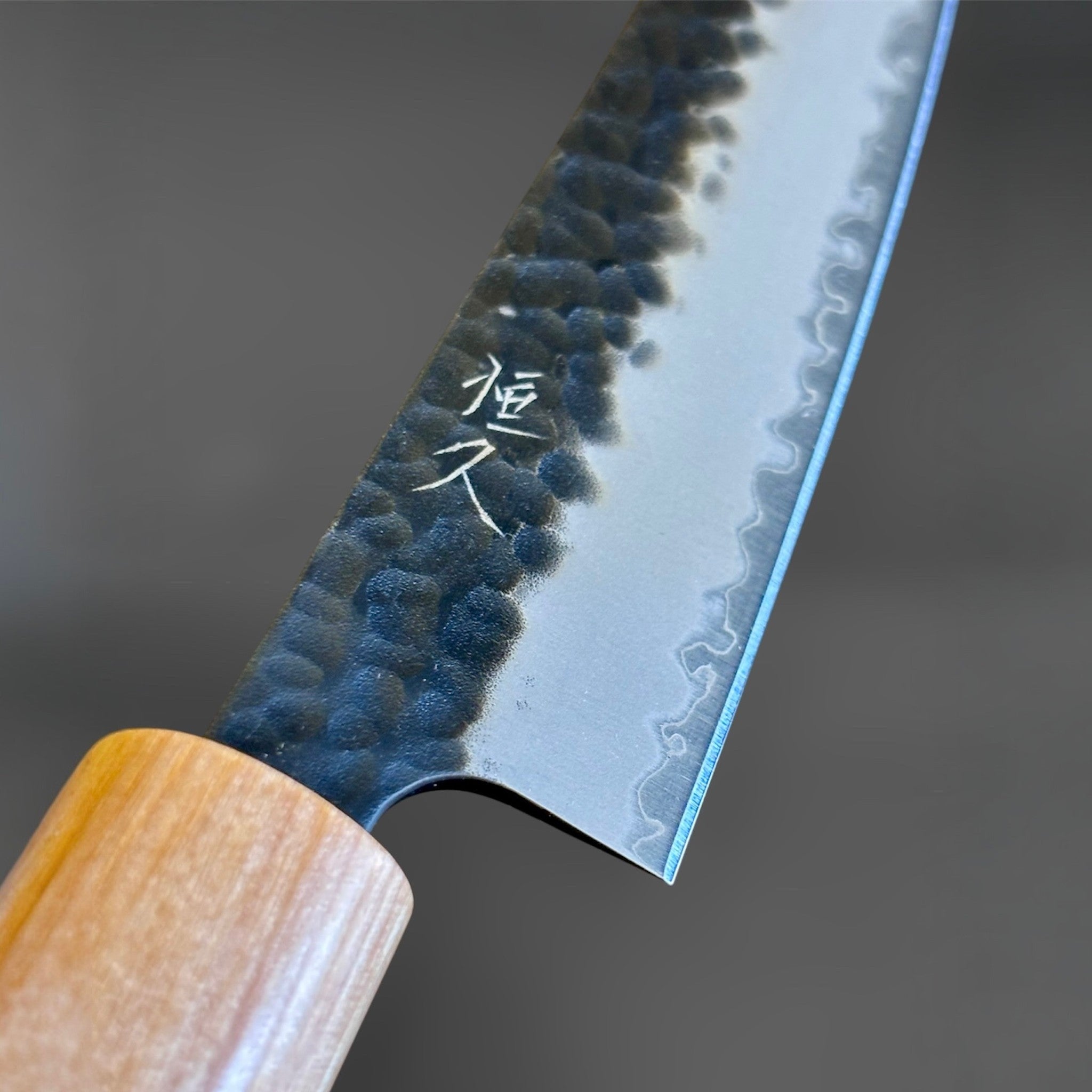 Tsunehisa Aogami Super Tsuchime Kuro Petty 150 mm with morado handle, close-up of the heel, kanji engraving, hammered kurouchi texture, and polished core steel cladding line.