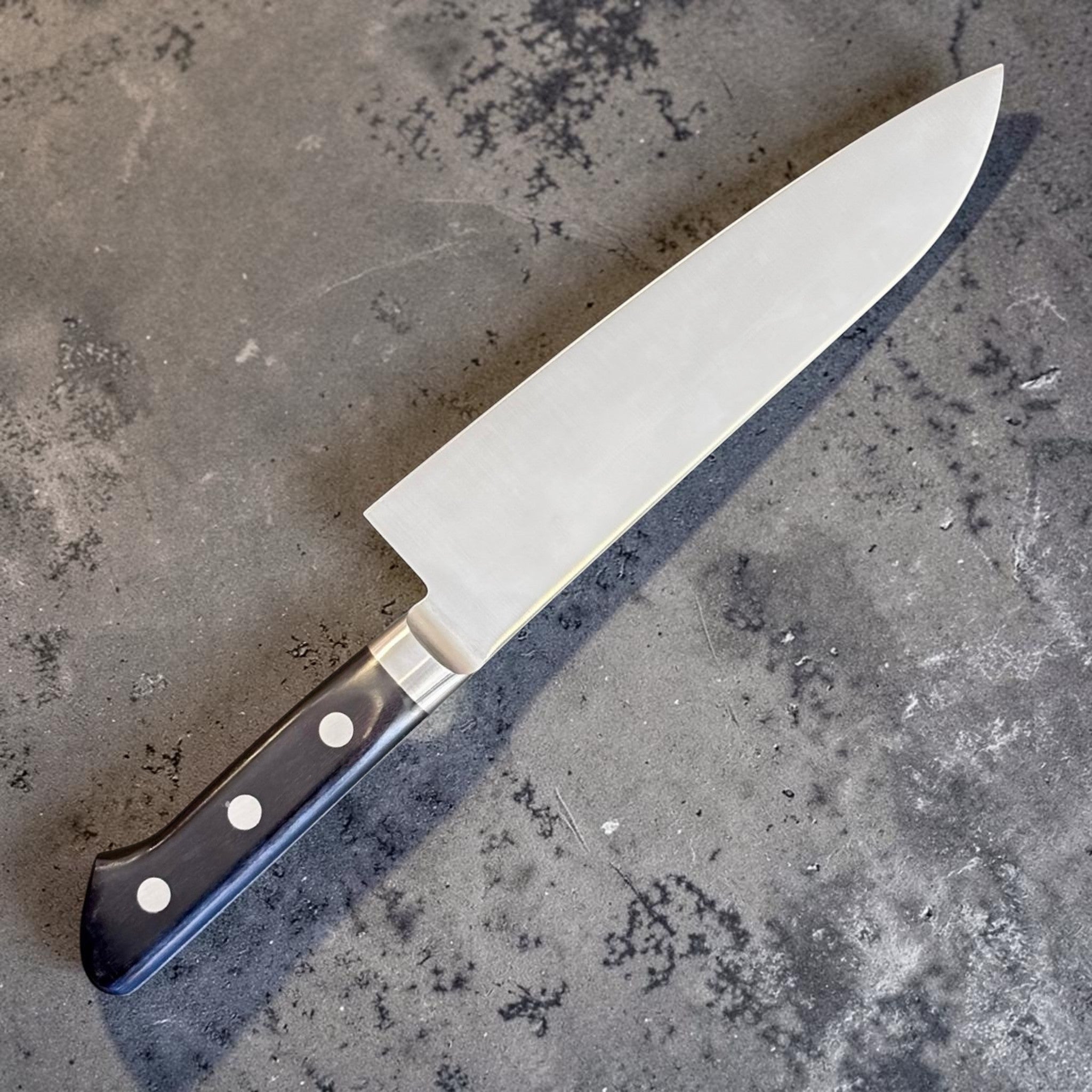 Tsunehisa Mono AUS-8 Santoku 165 mm with black Western handle, angled blade view with black Western handle and stainless bolster.