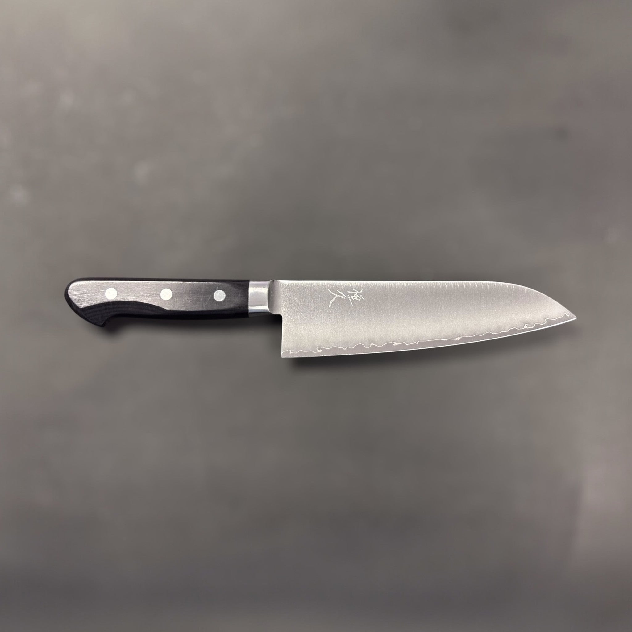 Tsunehisa VG-1 stainless steel Santoku 165 mm with black Western handle, medium distance side profile of the entire knife on grey background.