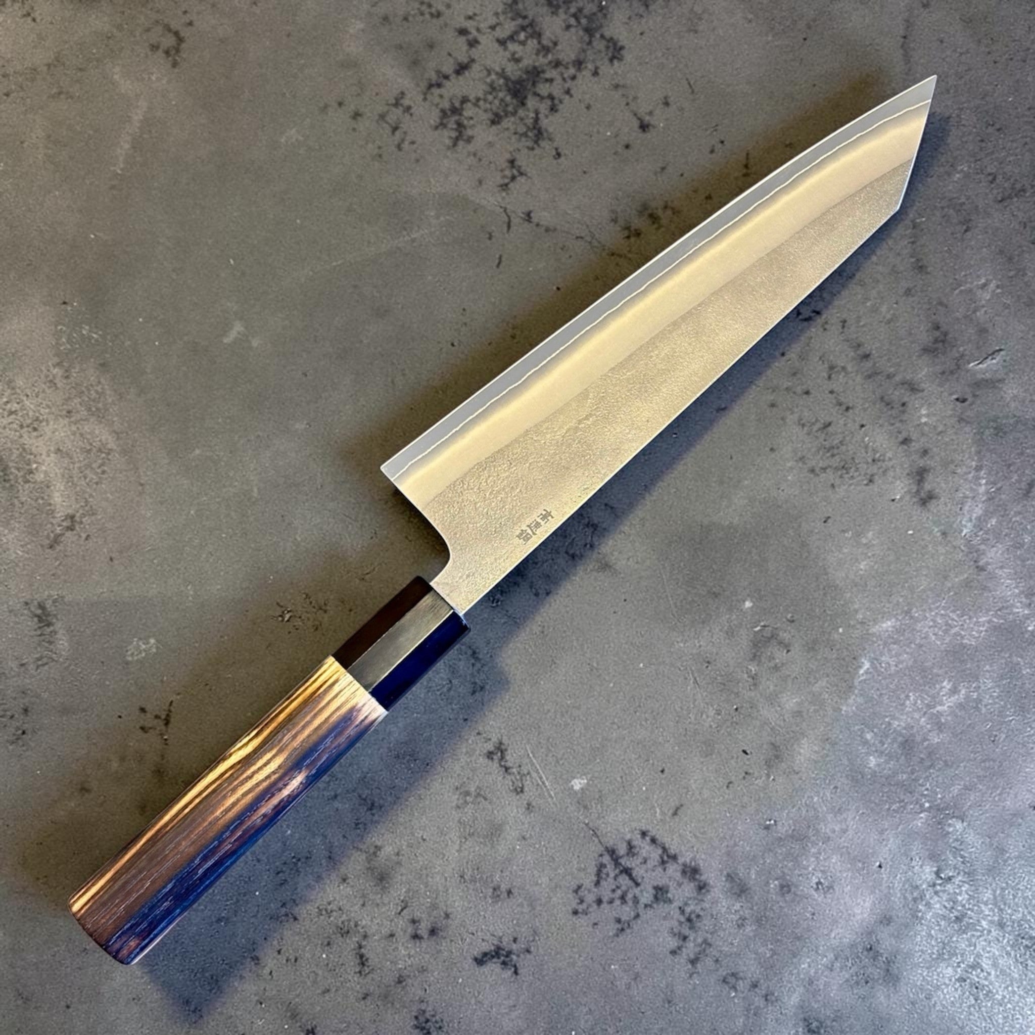 Yoshikane SKD Nashiji Kiritsuke 210 mm with burnt wood and black buffalo horn handle, reverse side angled view on gray background.