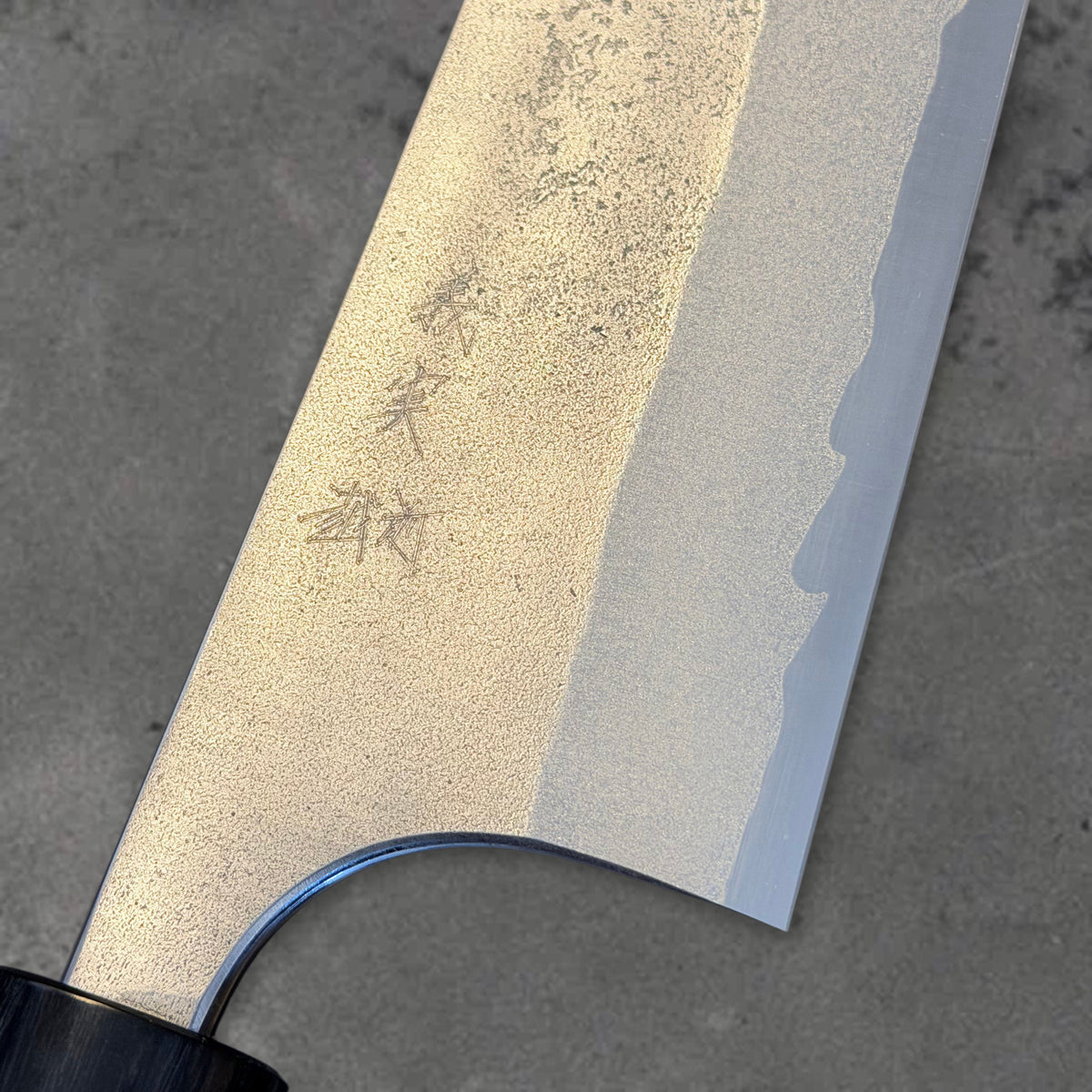 Close-up of the Yoshimi Kato Aogami Super Nashiji 240mm gyuto showing the engraved blade, nashiji texture, cladding line, and heel.