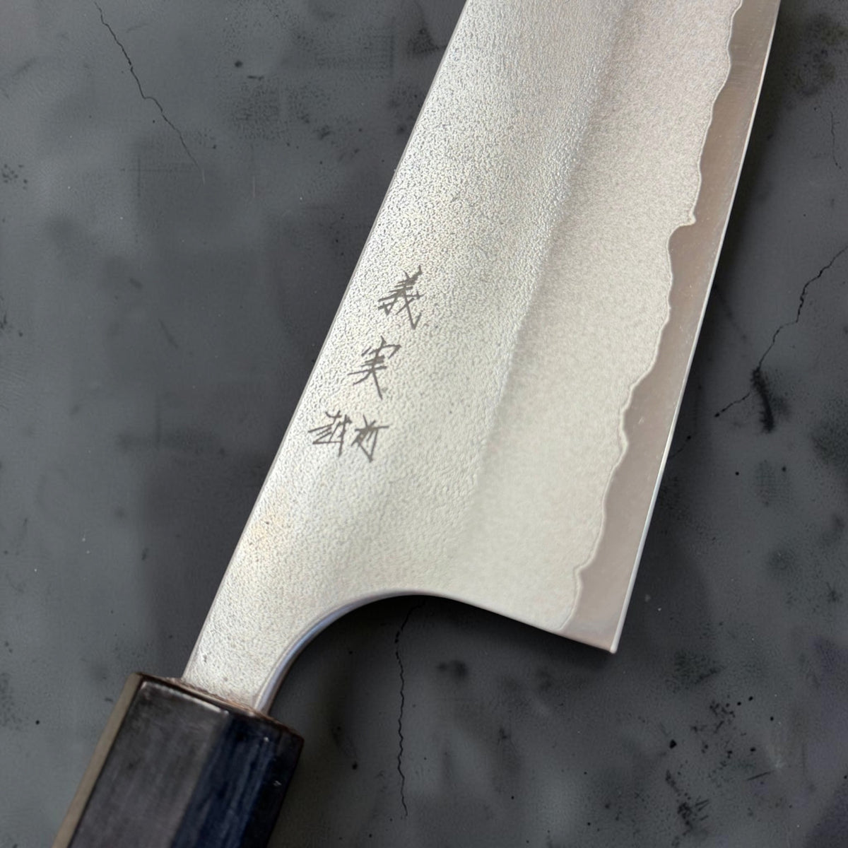 Close-up of the Yoshimi Kato 240mm gyuto showing kanji, Nashiji texture, cladding line and curved choil.