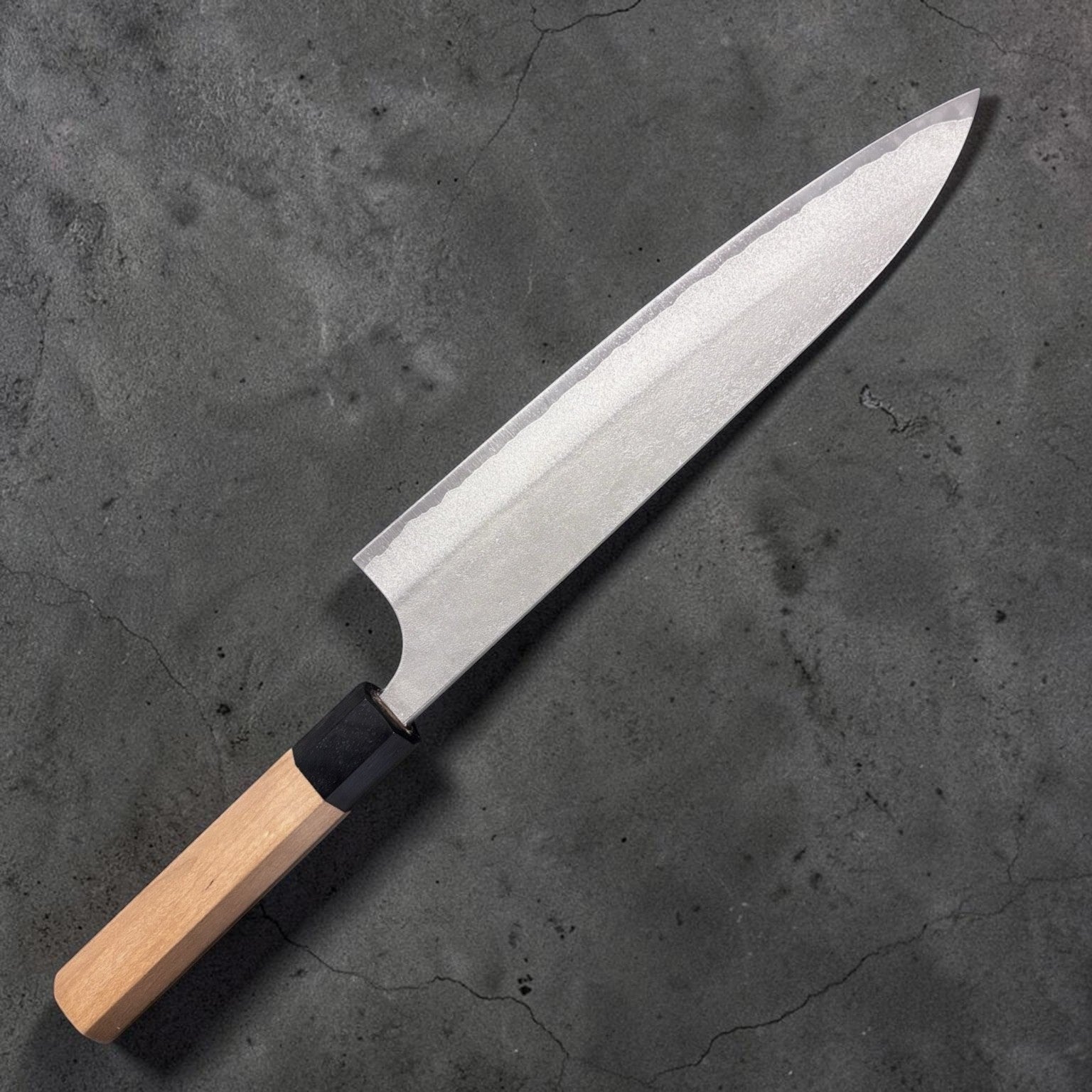 Yoshimi Kato AS Nashiji Gyuto 240mm, angled shot highlighting edge geometry and forged Nashiji pattern.