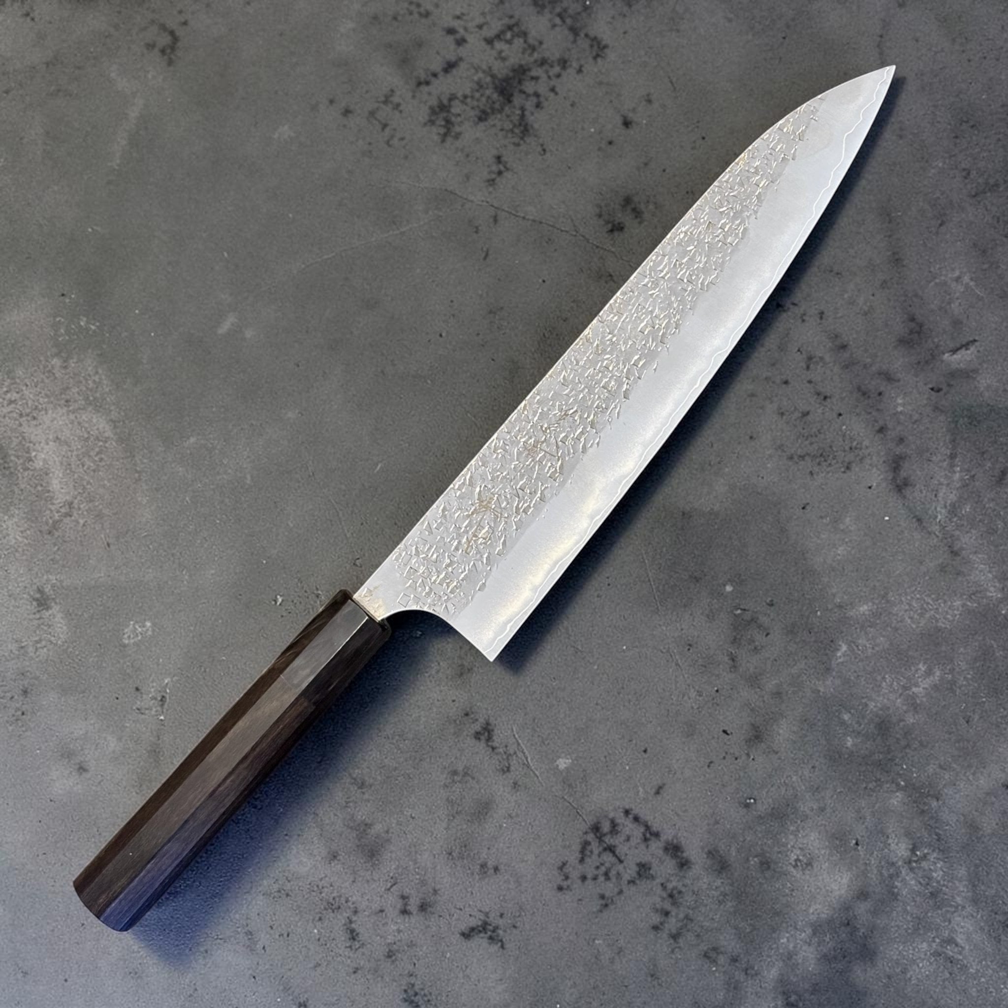 Yu Kurosaki Shizuku SG2 Gyuto 240 mm with ebony and black horn handle, angled full knife view showing hammered shizuku texture and polished blade.