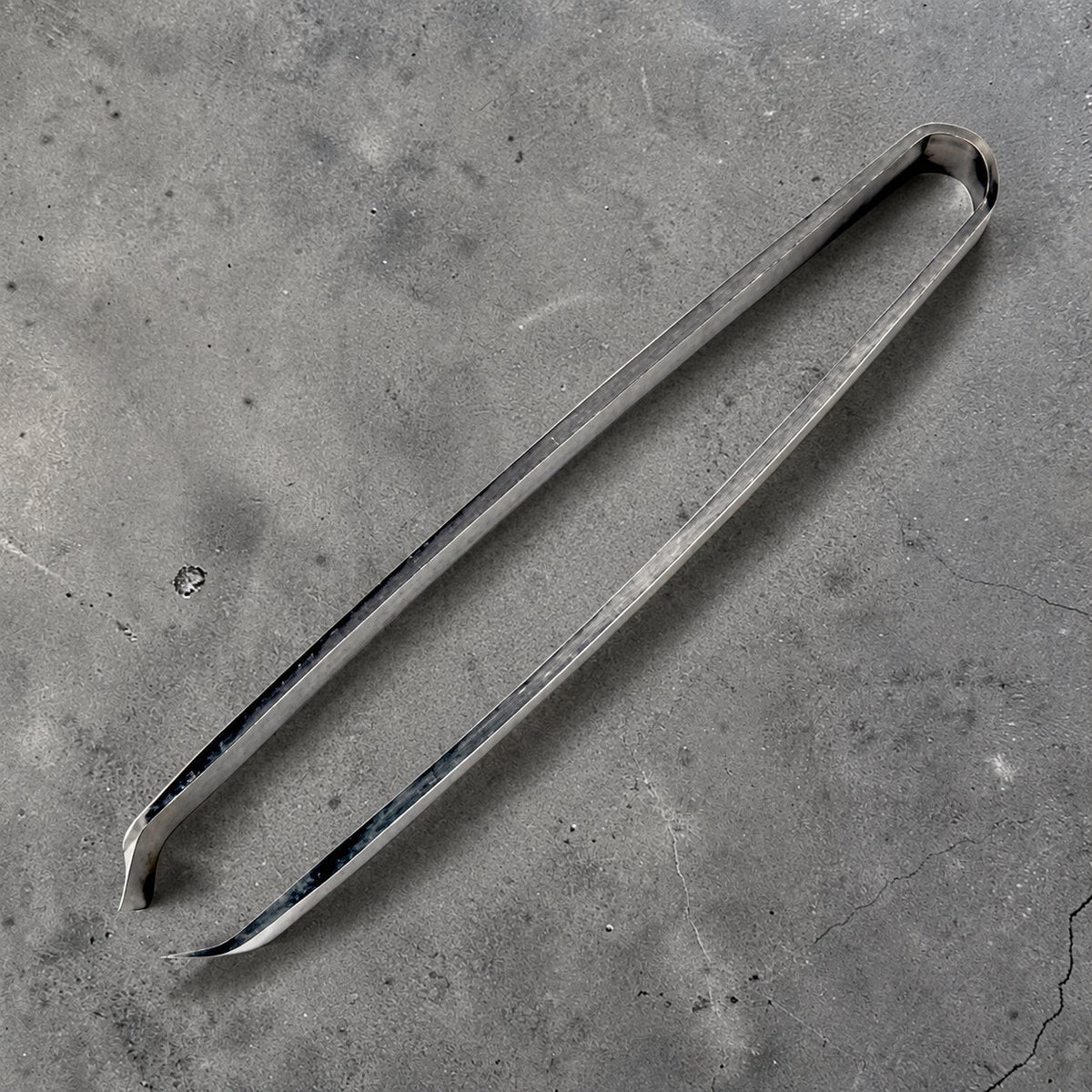 Small stainless steel fish bone tweezers, open side view on gray concrete