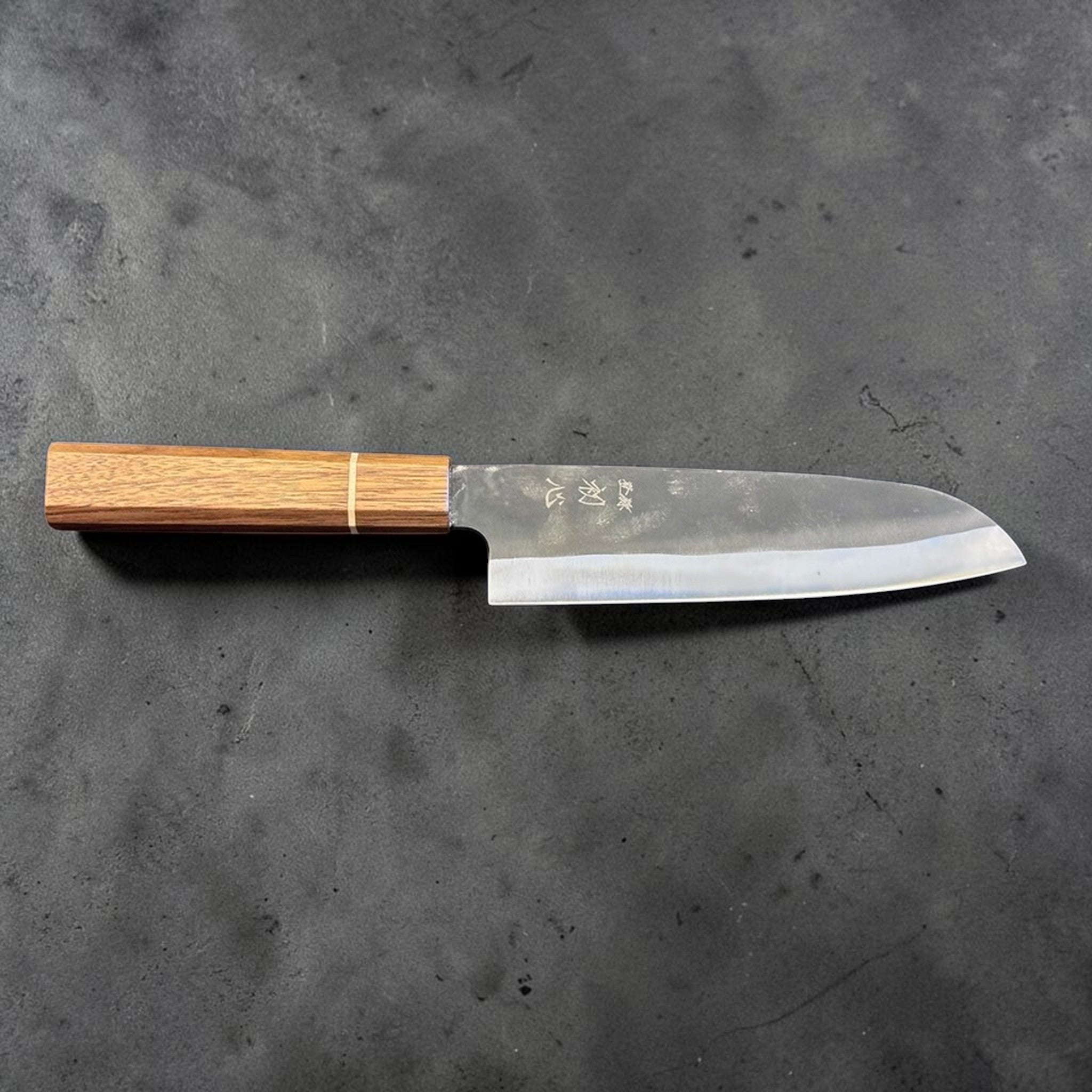 Hatsukokoro Aokitae Blue #2 Kurouchi Santoku 180 mm with Sanjo walnut handle and maple stripe, angled back side view showing the grind and blade profile.