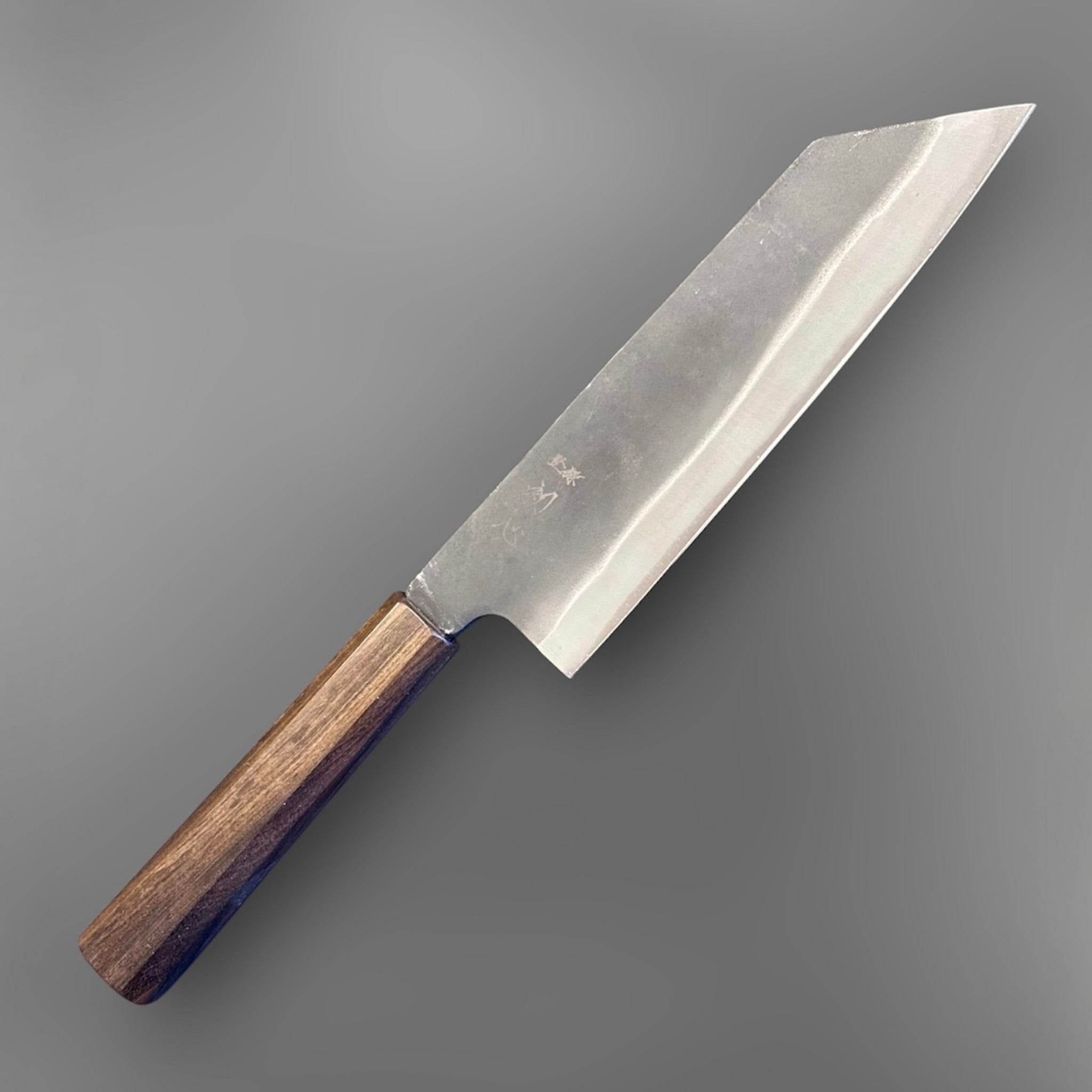 Hatsukokoro Blue #2 Kurouchi Bunka 190 mm with mono ebony handle, angled front-side product photo showing the dark kurouchi finish, wide bevel, and aggressive k-tip bunka profile.