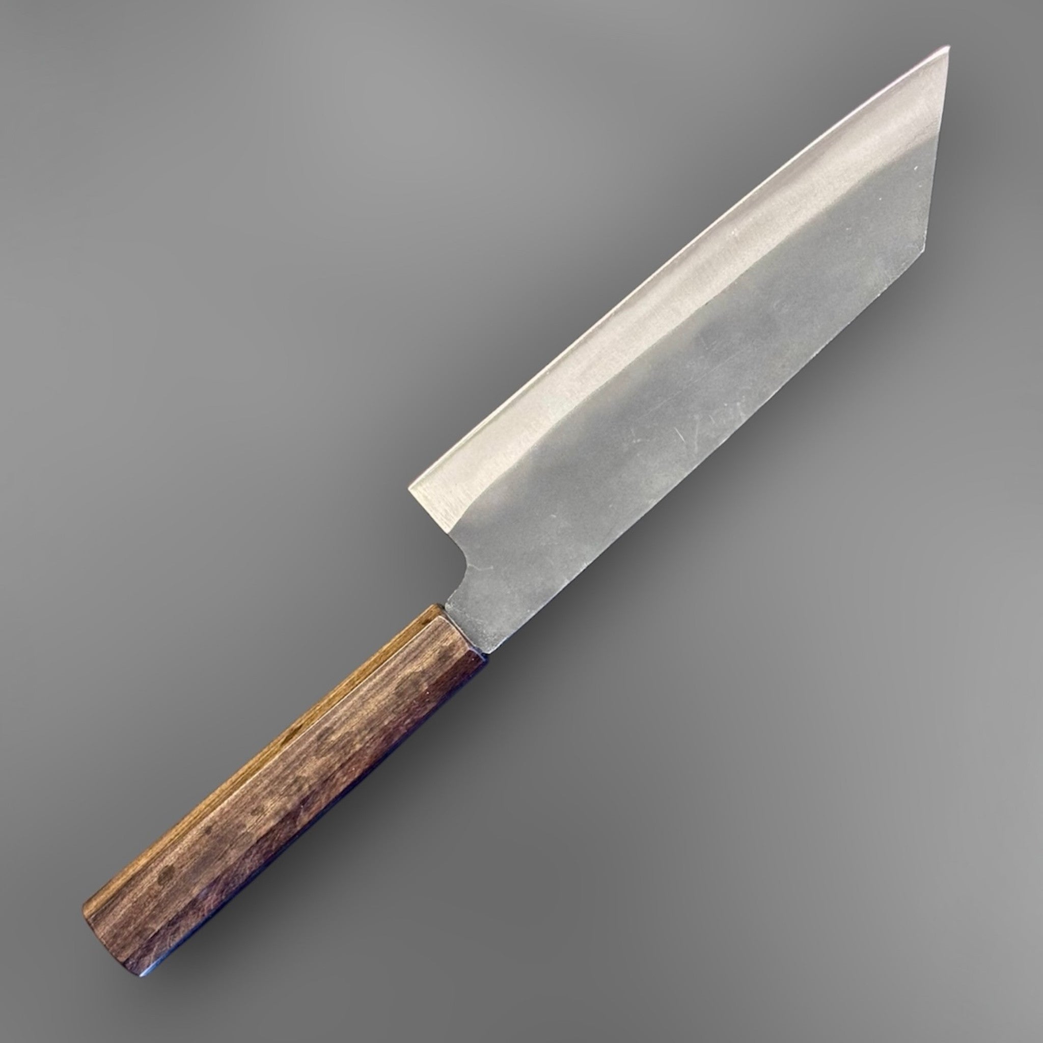 Hatsukokoro Blue #2 Kurouchi Bunka 190 mm with mono ebony handle, angled back-side product photo highlighting the rustic kurouchi blade road, tall heel, and faceted octagonal ebony wa handle.