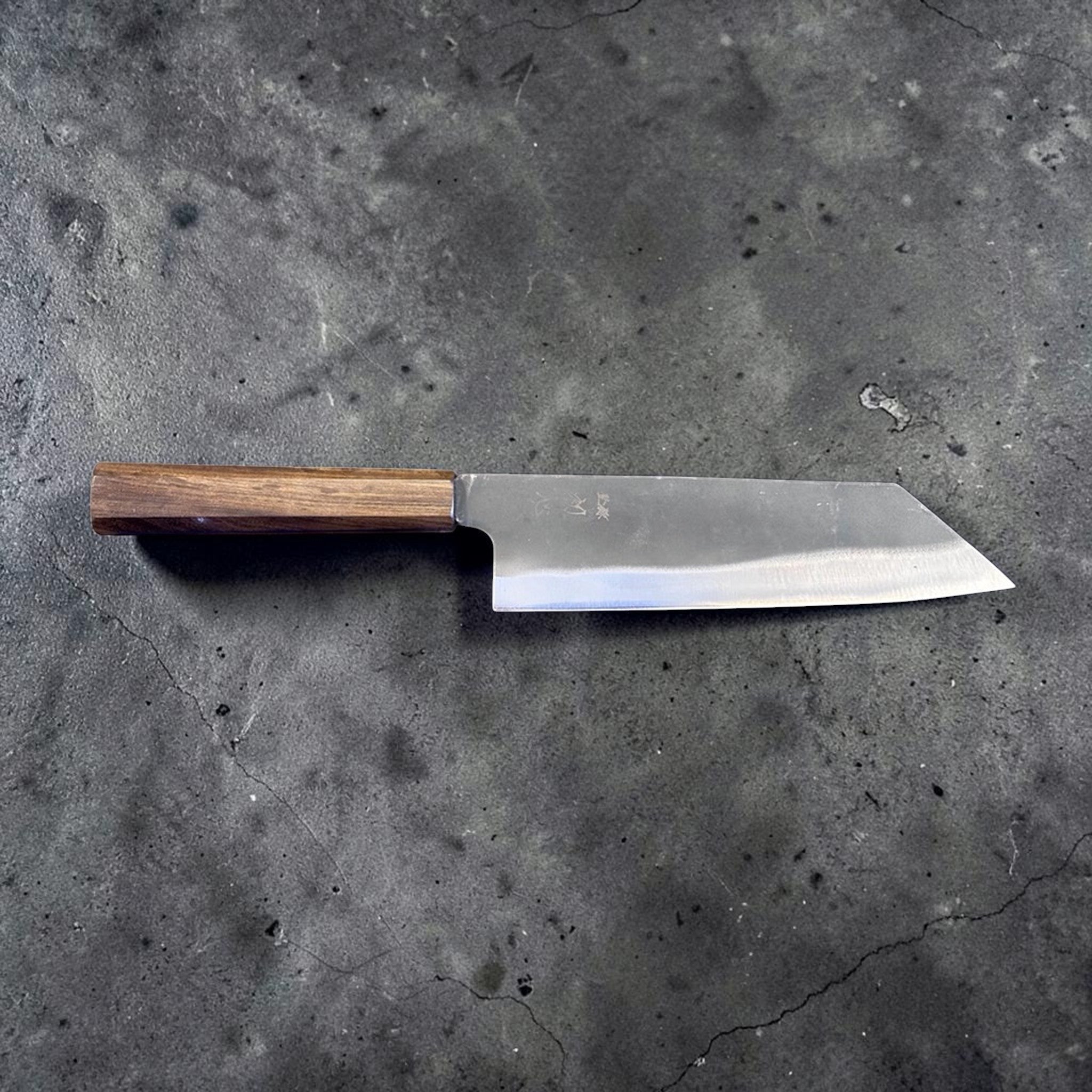 Hatsukokoro Blue #2 Kurouchi Bunka 190 mm with mono ebony handle, full profile front-side view on gray background showing the long bunka edge line, pronounced reverse tanto tip, and traditional wa handle.