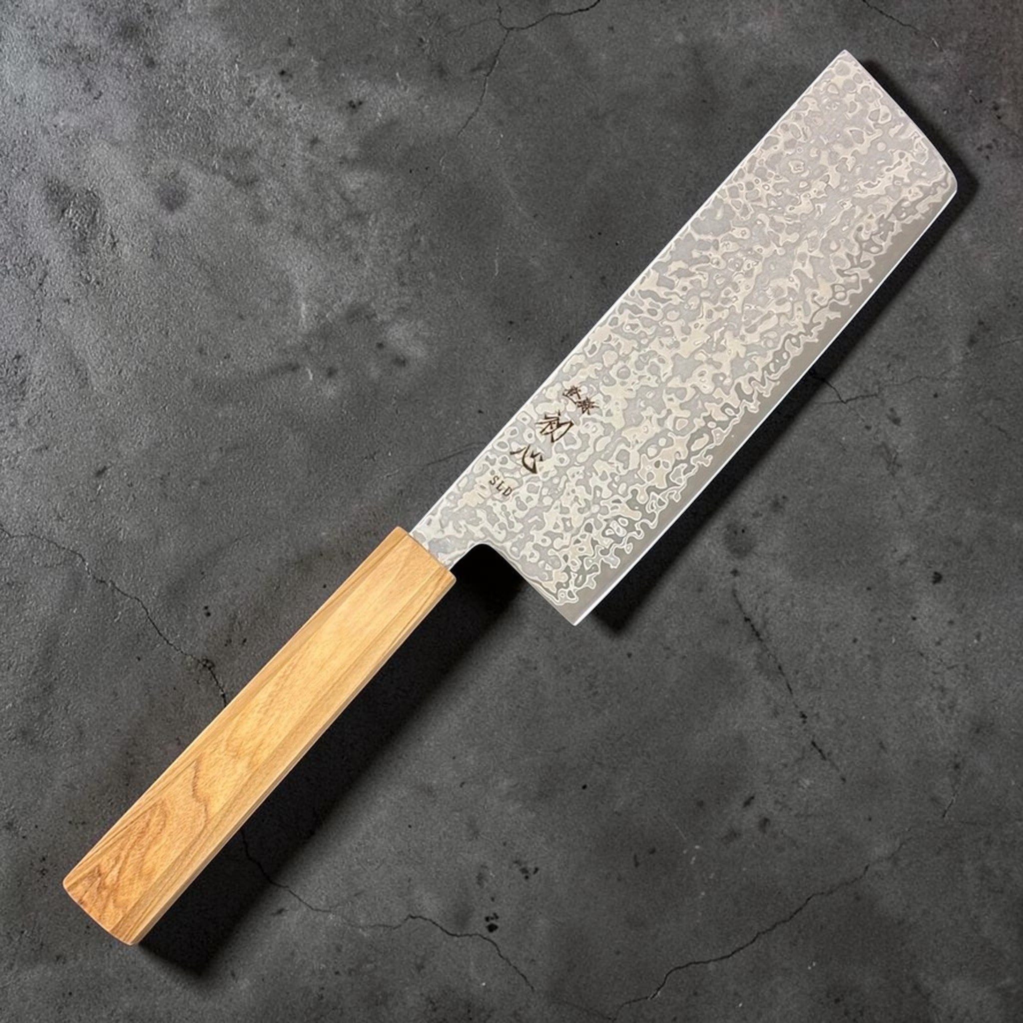 Hatsukokoro Hikari SLD Damascus Nakiri 160 mm with olive wood handle, angled hero shot.