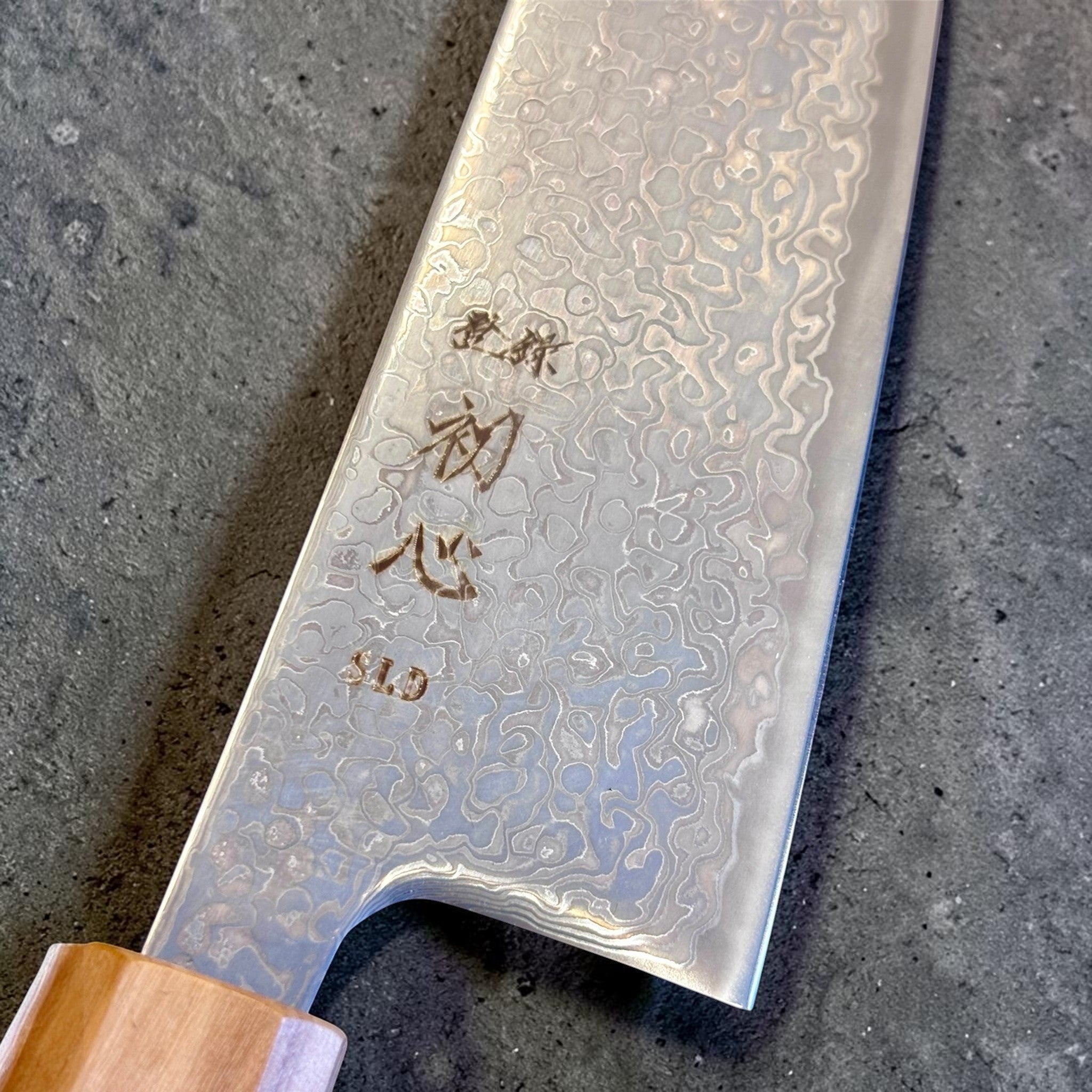 Hatsukokoro Hikari SLD Damascus Kurozome Bunka 170 mm with olive wood handle, close-up of kuro-zome damascus pattern and engraved blade details.