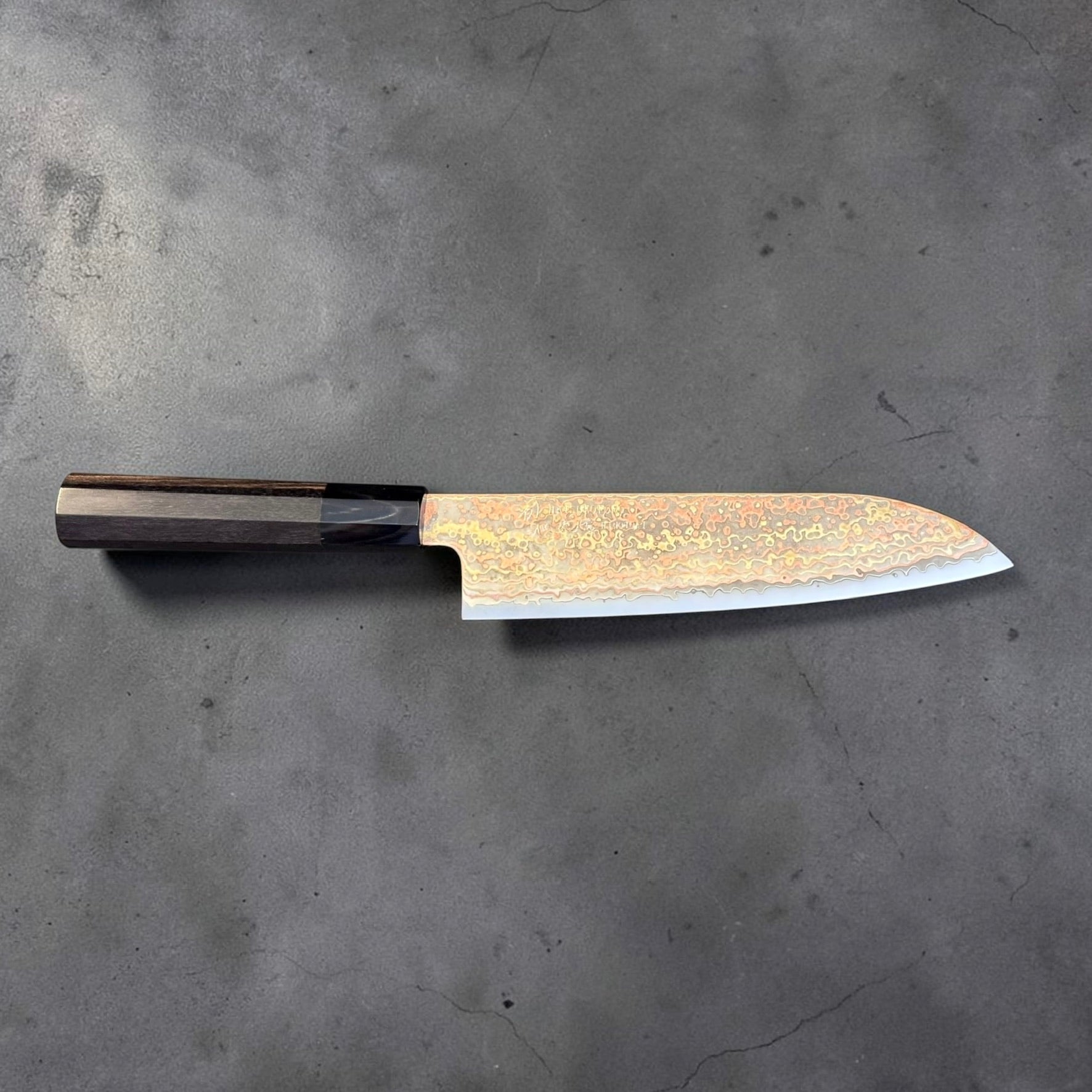 Reverse side of Hatsukokoro Hinotori V-Toku 2 rainbow Damascus Santoku with ebony and black horn handle