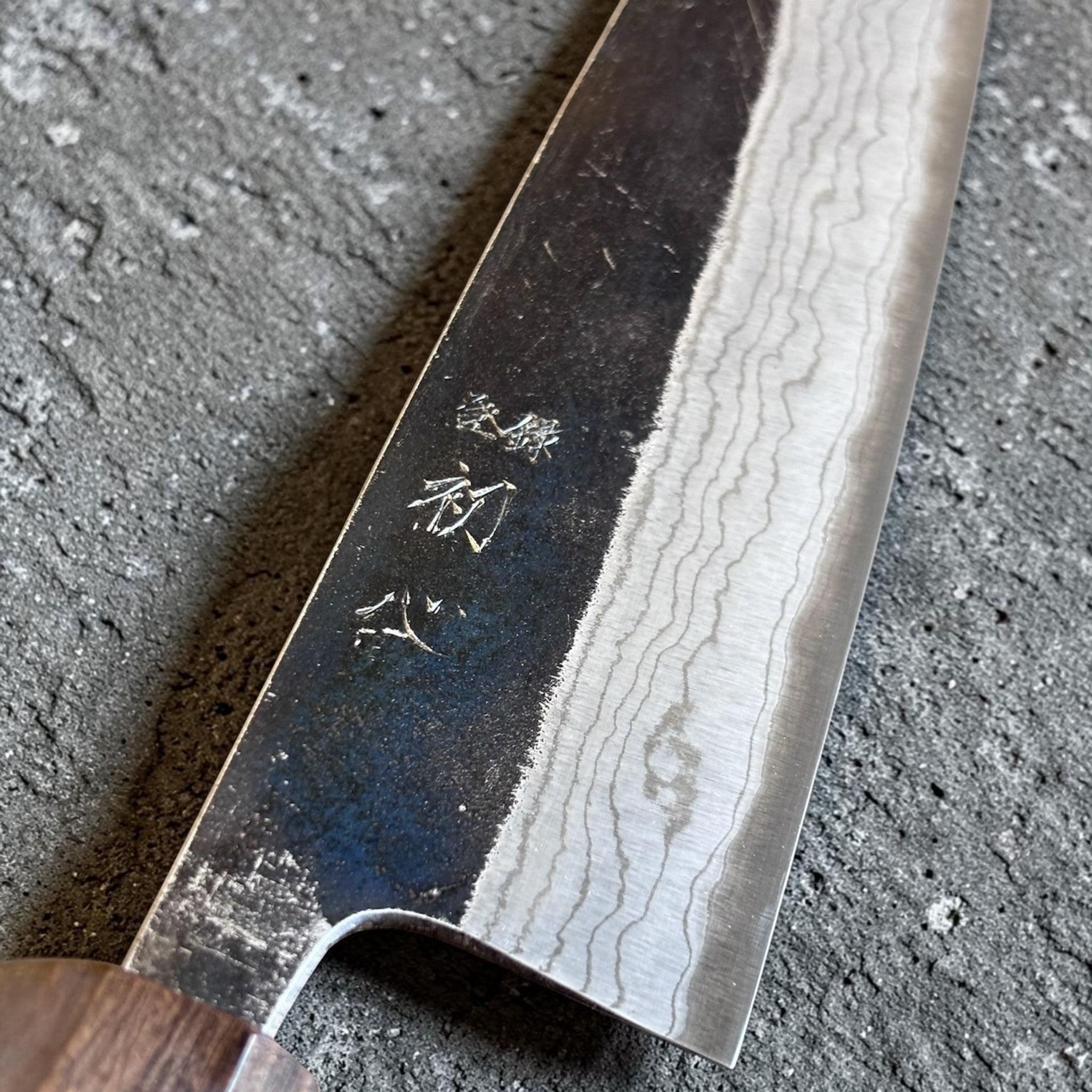 Hatsukokoro Kumokage Blue #2 Gyuto 240 mm with mono ebony handle, close-up of the kurouchi and layered blade pattern.