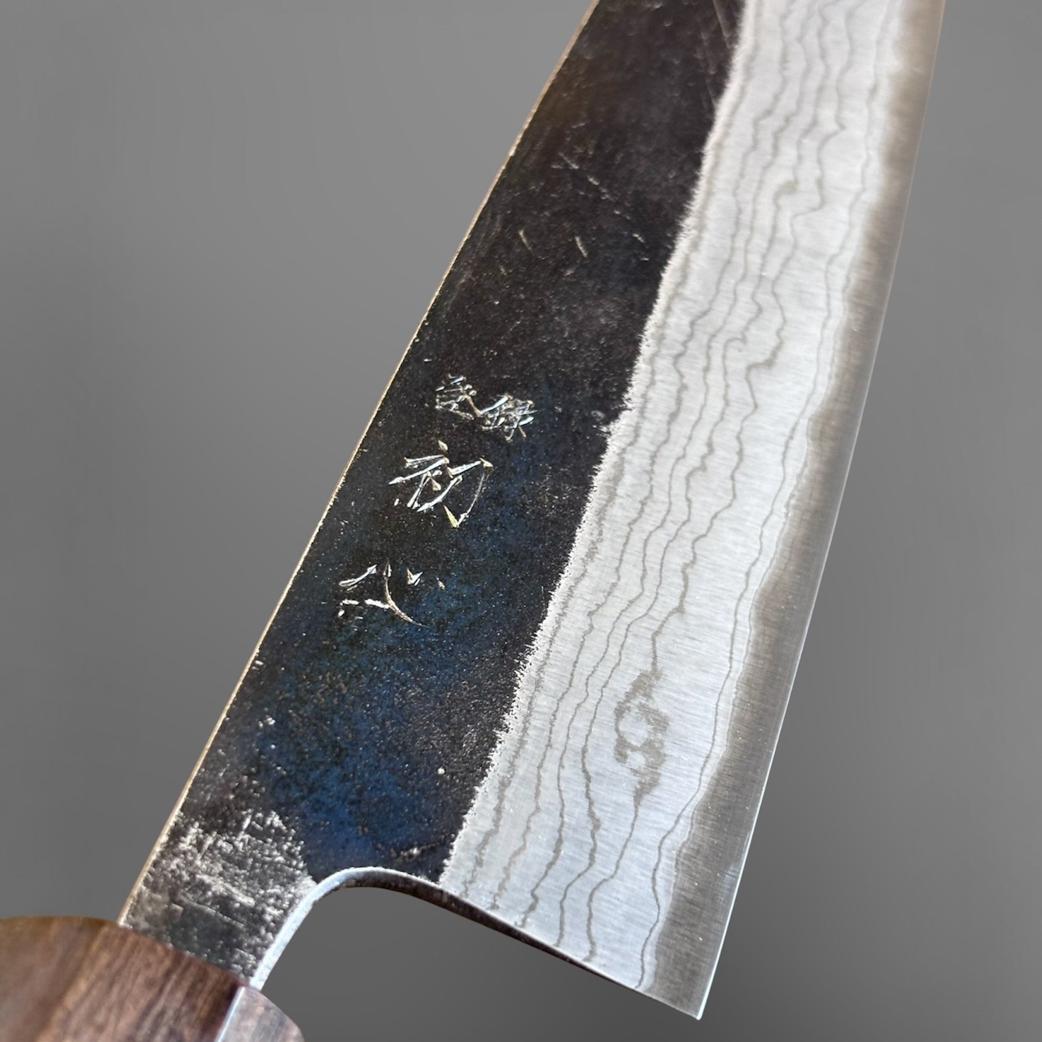 Hatsukokoro Kumokage Blue #2 Gyuto 240 mm with mono ebony handle, close-up of the kurouchi and layered blade pattern.