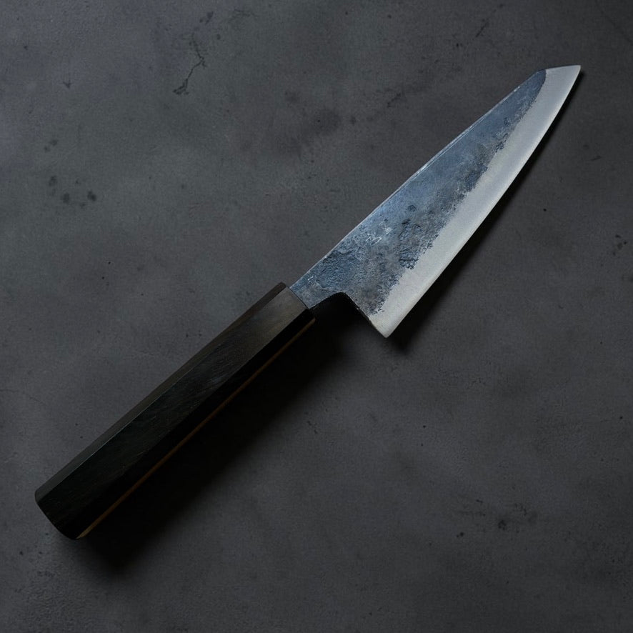 Hatsukokoro Kurogane Blue #2 Kurouchi Honesuki 150mm with mono ebony handle, kanji-side angled view.
