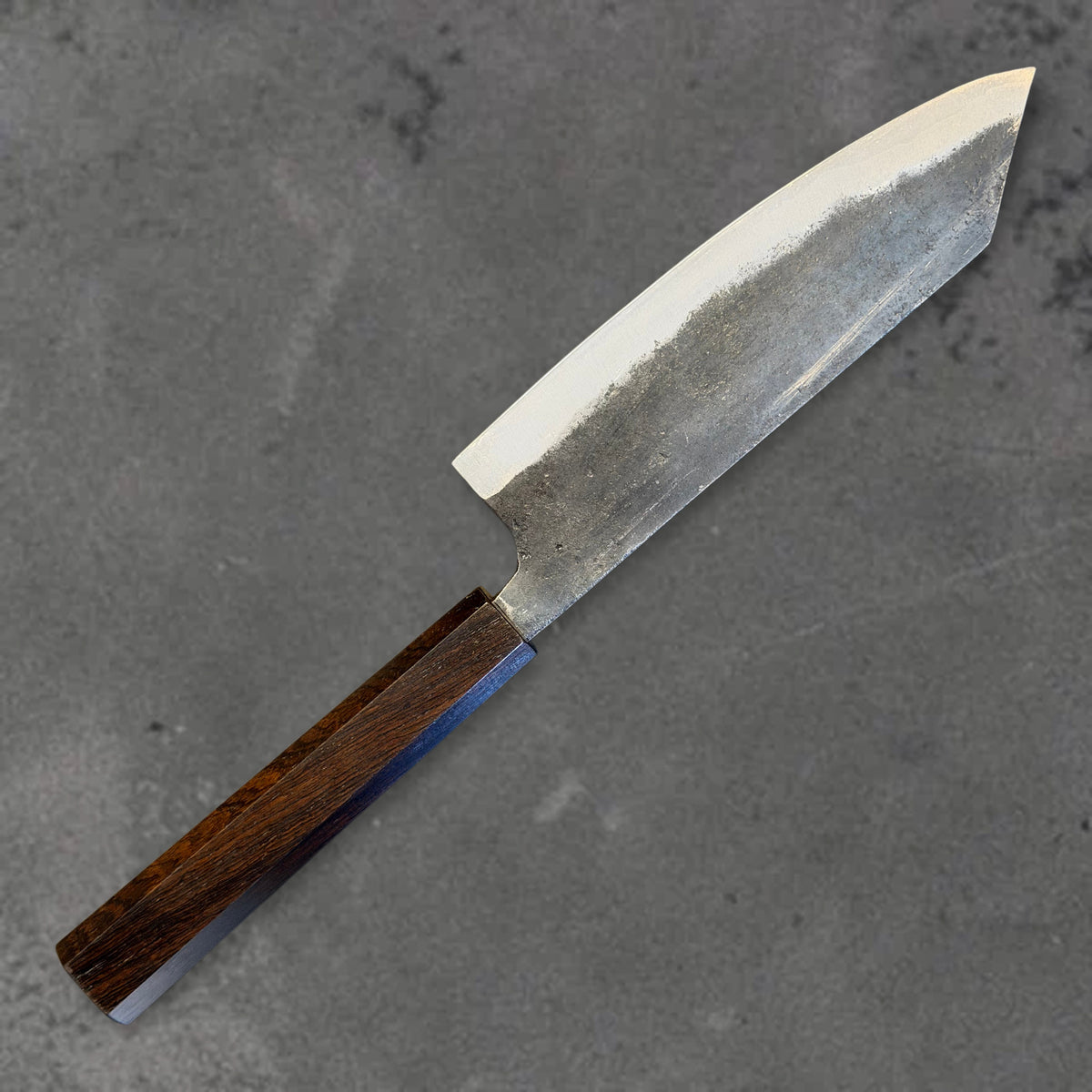 Angled reverse view of the Hatsukokoro Kurogane Blue #2 Kurouchi 165mm bunka with ebony handle, showing the blade shape, finish, and handle.