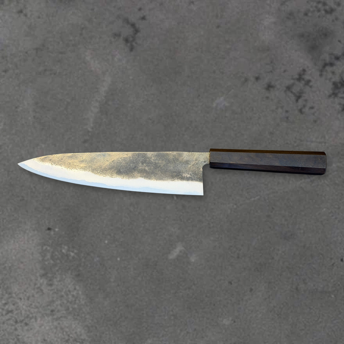 Hatsukokoro Kurogane Blue #2 Kurouchi 210mm gyuto with ebony handle, shown in horizontal reverse profile with the full blade and handle visible.