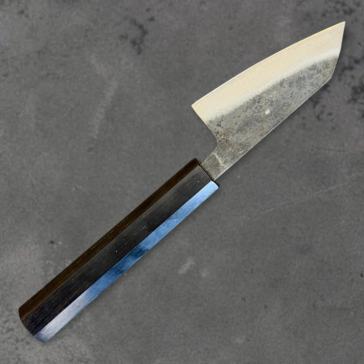 Angled reverse view of the Hatsukokoro Kurogane Blue #2 Kurouchi 80mm ko-bunka with ebony handle, showing the blade shape, finish, and handle.