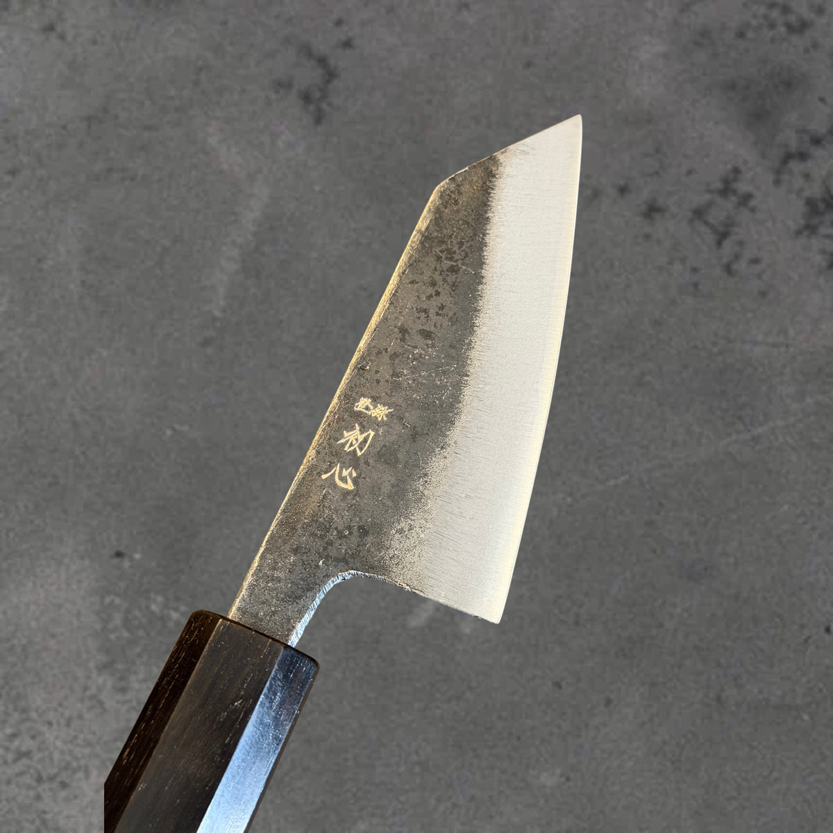 Close-up of the Kurouchi finish, blade markings, and polished bevel on the Hatsukokoro Kurogane Blue #2 Kurouchi 80mm ko-bunka with ebony handle.