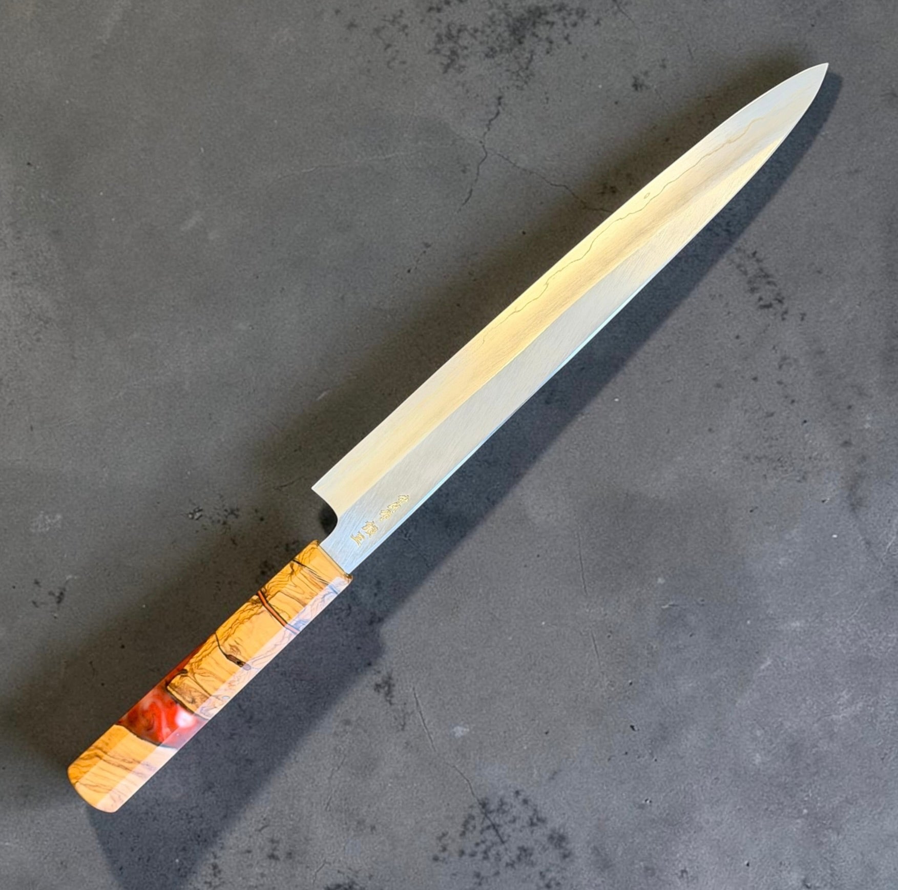 Angled blade view of Hatsukokoro Nakagawa Ginsan Sujihiki 270mm showing its polished wide bevel and fine slicing tip