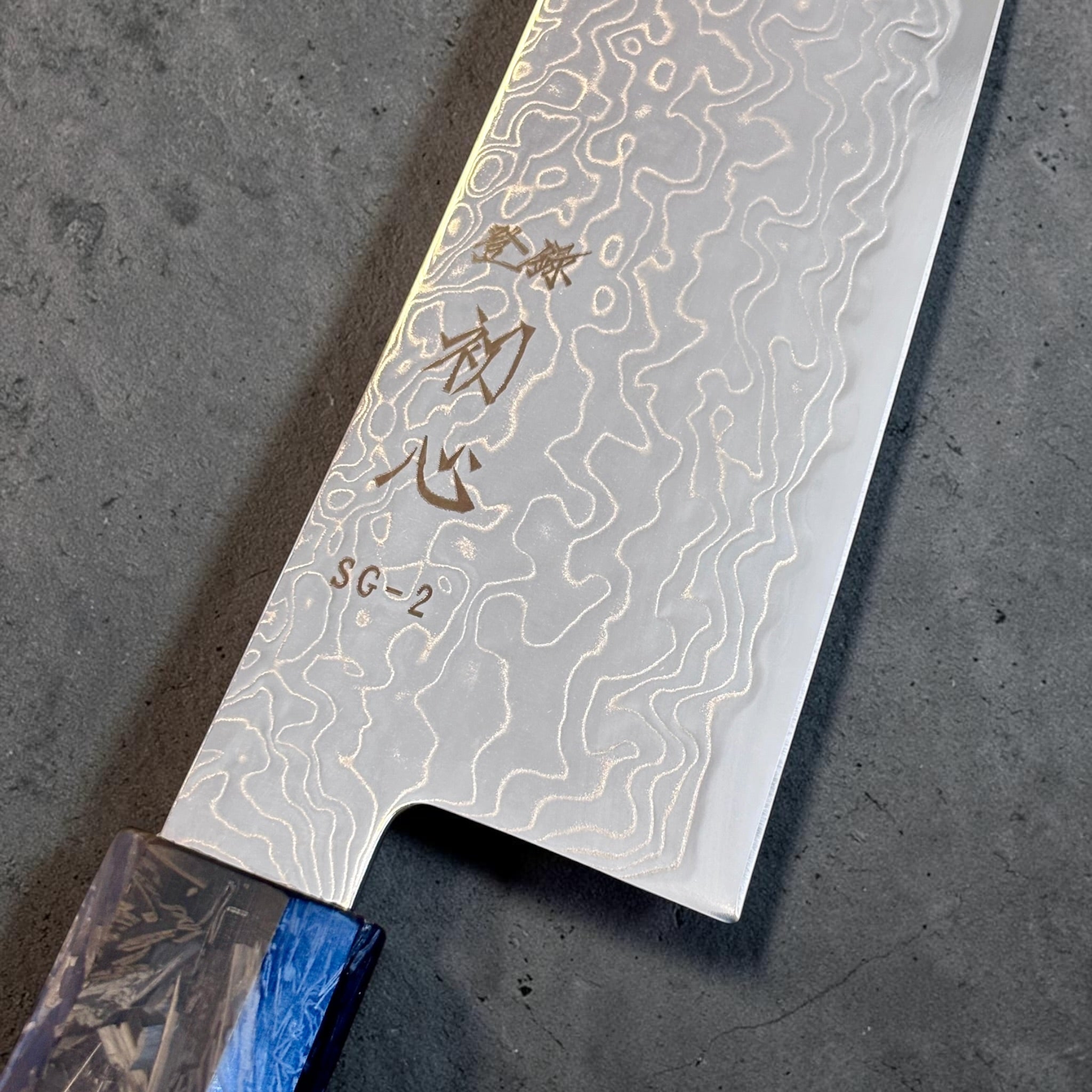 Close-up of the Ryuhyo Damascus pattern, Hatsukokoro kanji, and SG2 engraving on the 210mm gyuto.