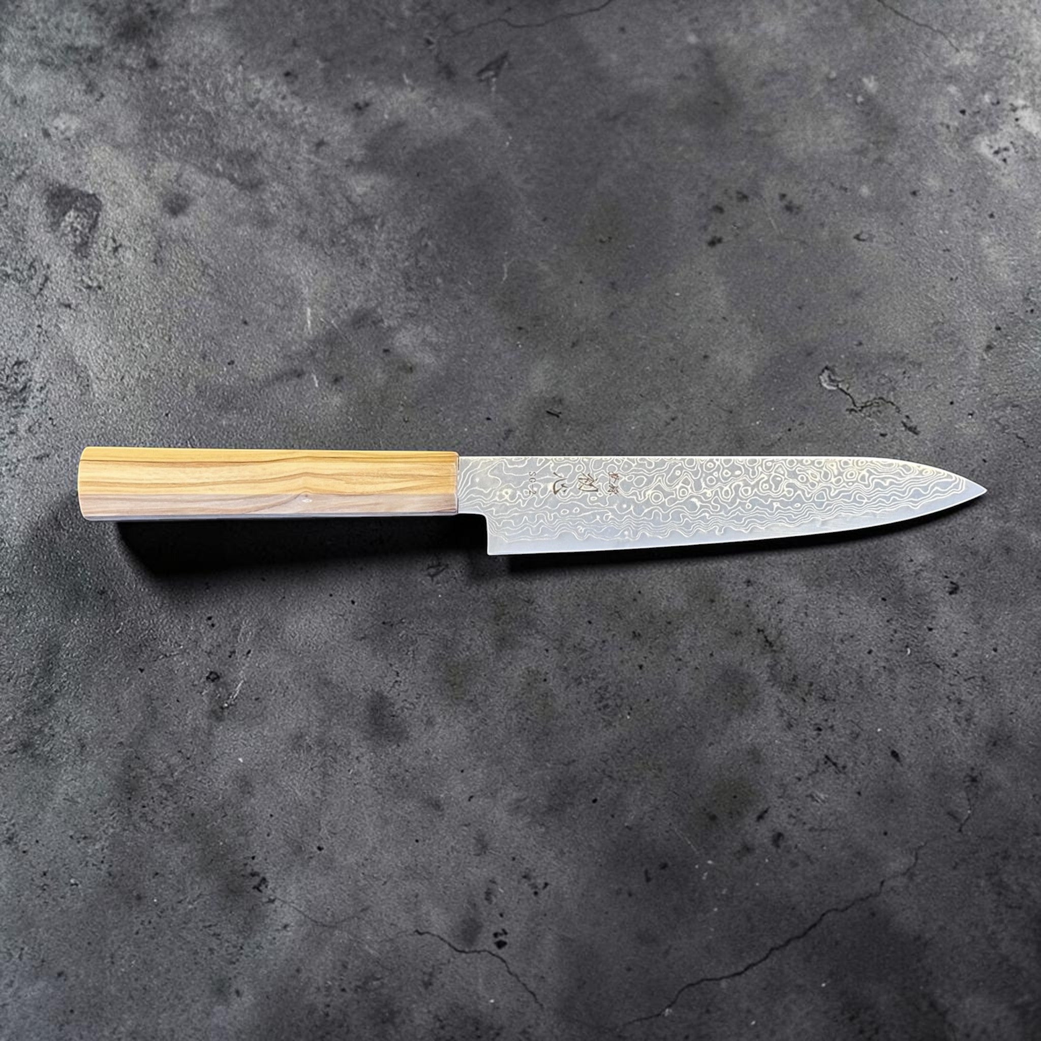 Hatsukokoro Ryuhyo SG2 Damascus Petty 150 mm with olive wood handle, full side profile showing the flowing Damascus blade pattern.