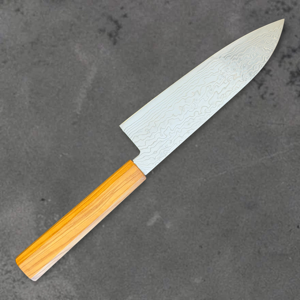 Angled reverse view of the Hatsukokoro Ryuhyo SG2 Damascus santoku with olive wood handle, showing the blade shape, finish, and handle.