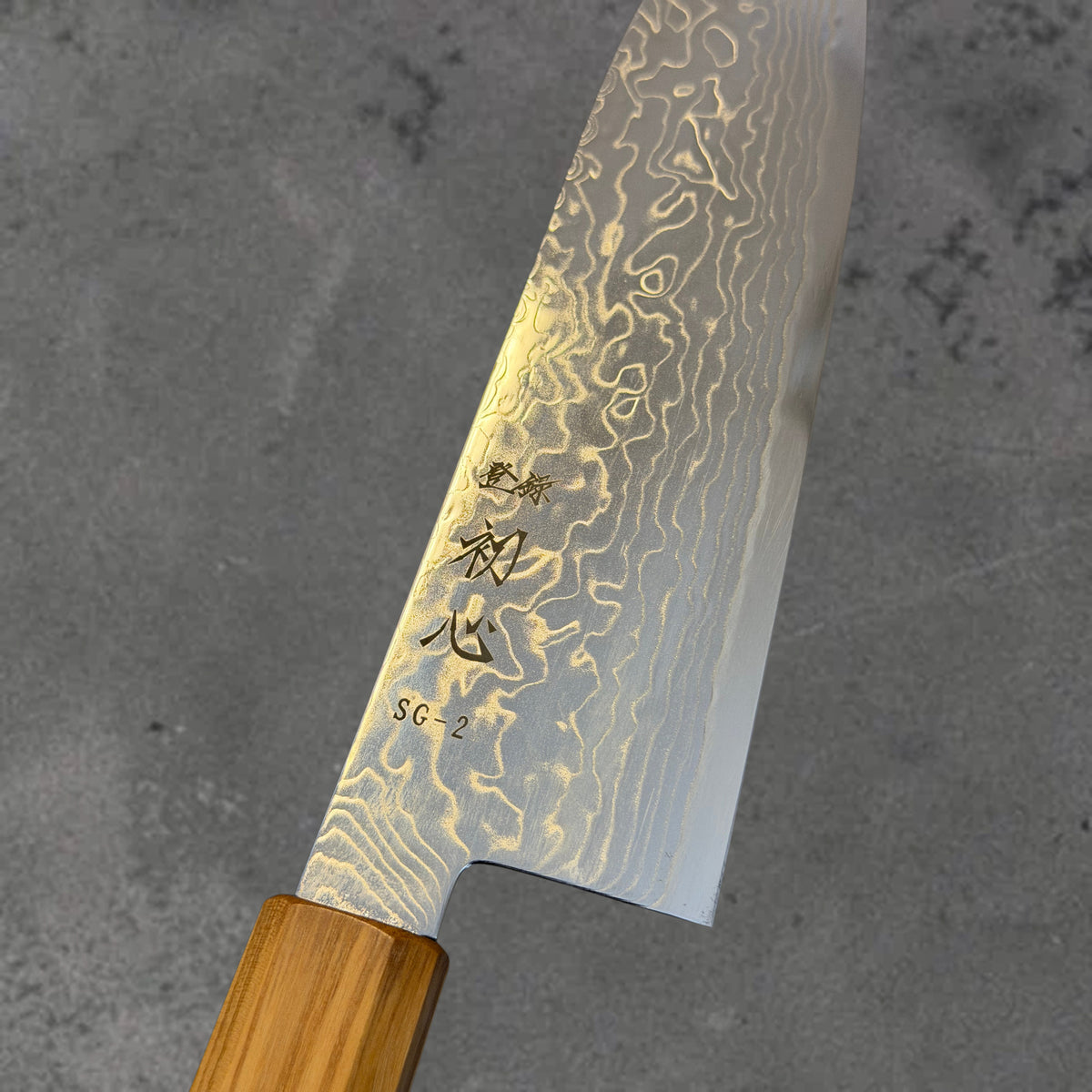 Close-up of the Damascus pattern and blade markings on the Hatsukokoro Ryuhyo SG2 Damascus santoku with olive wood handle.