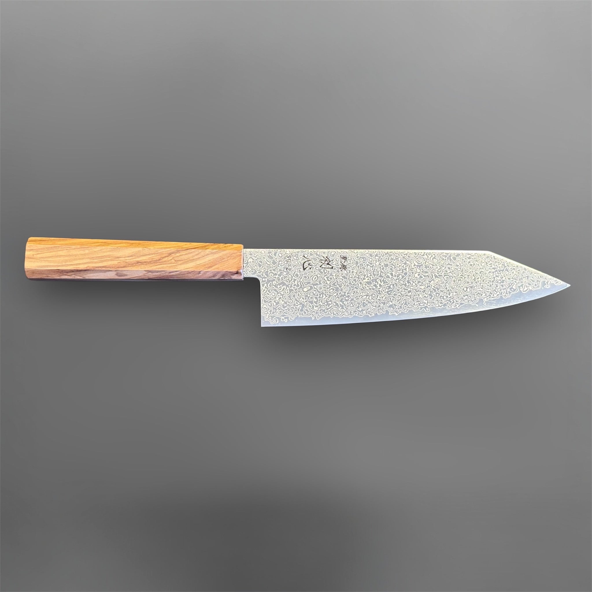 Hatsukokoro Saihyo SG2 Damascus Bunka 180 mm with olivewood handle, angled front-side view highlighting the Damascus pattern and profile.