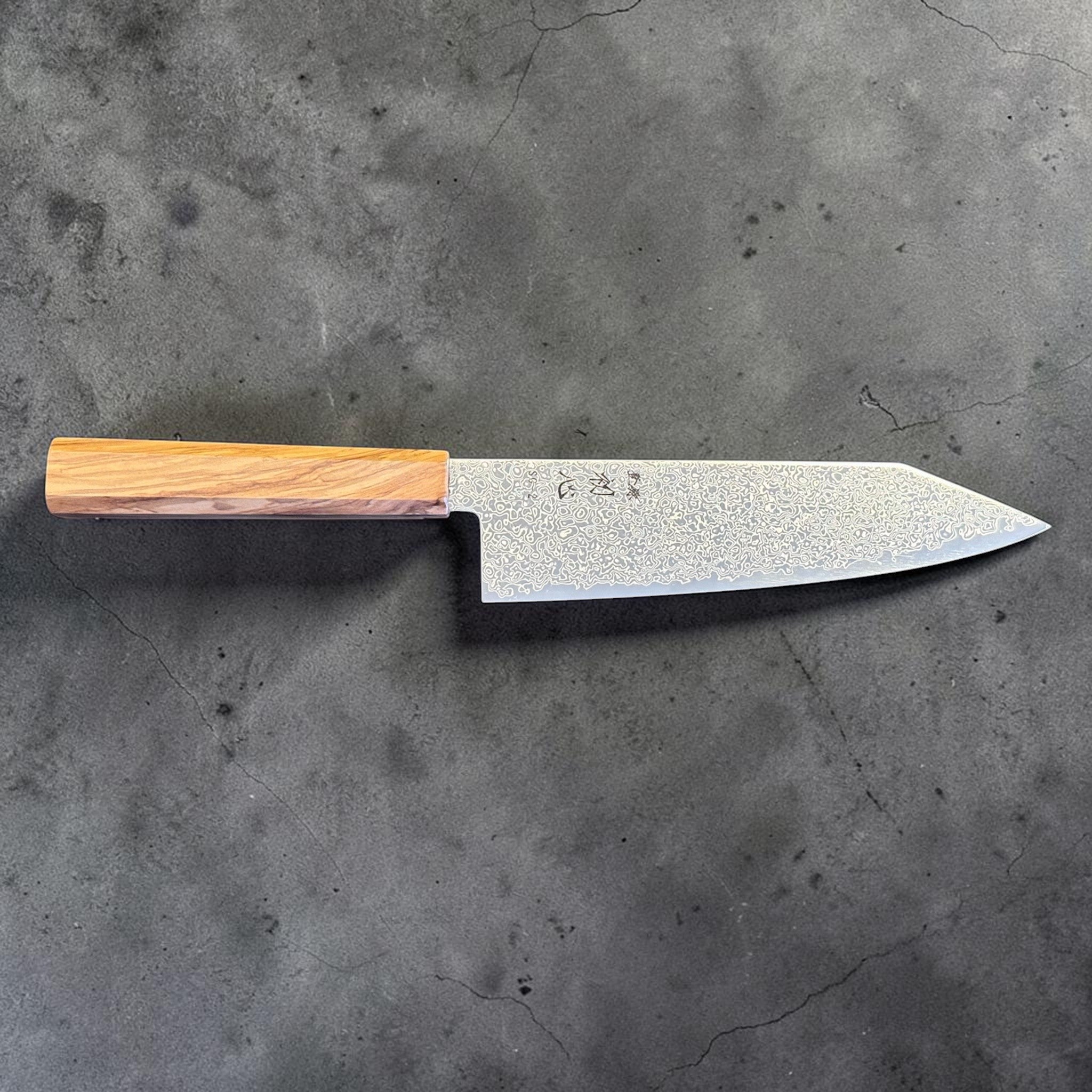 Hatsukokoro Saihyo SG2 Damascus Bunka 180 mm with olivewood handle, angled front-side view highlighting the Damascus pattern and profile.