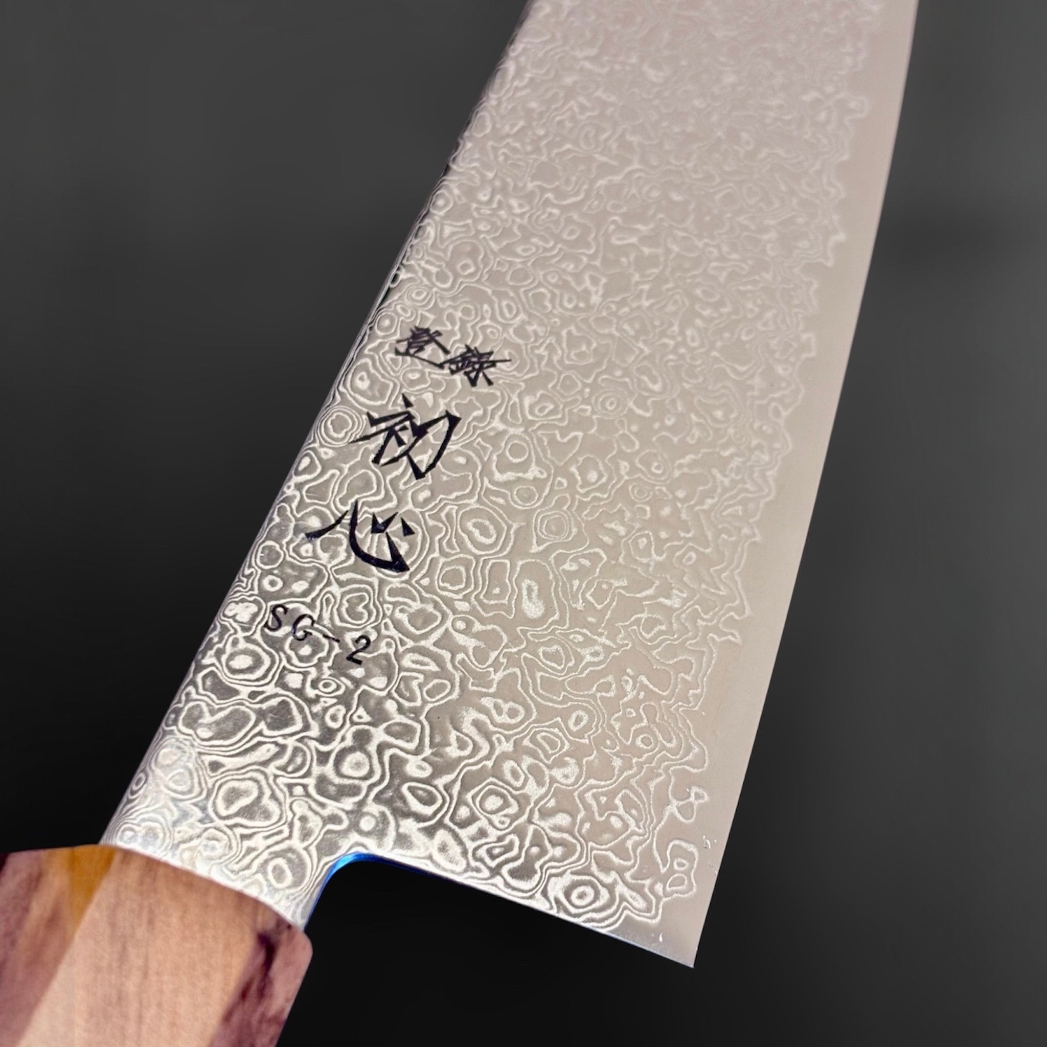 Hatsukokoro Saihyo SG2 Damascus Bunka 180 mm, close-up of the SG2 Damascus pattern, kanji engraving, and olivewood handle junction.