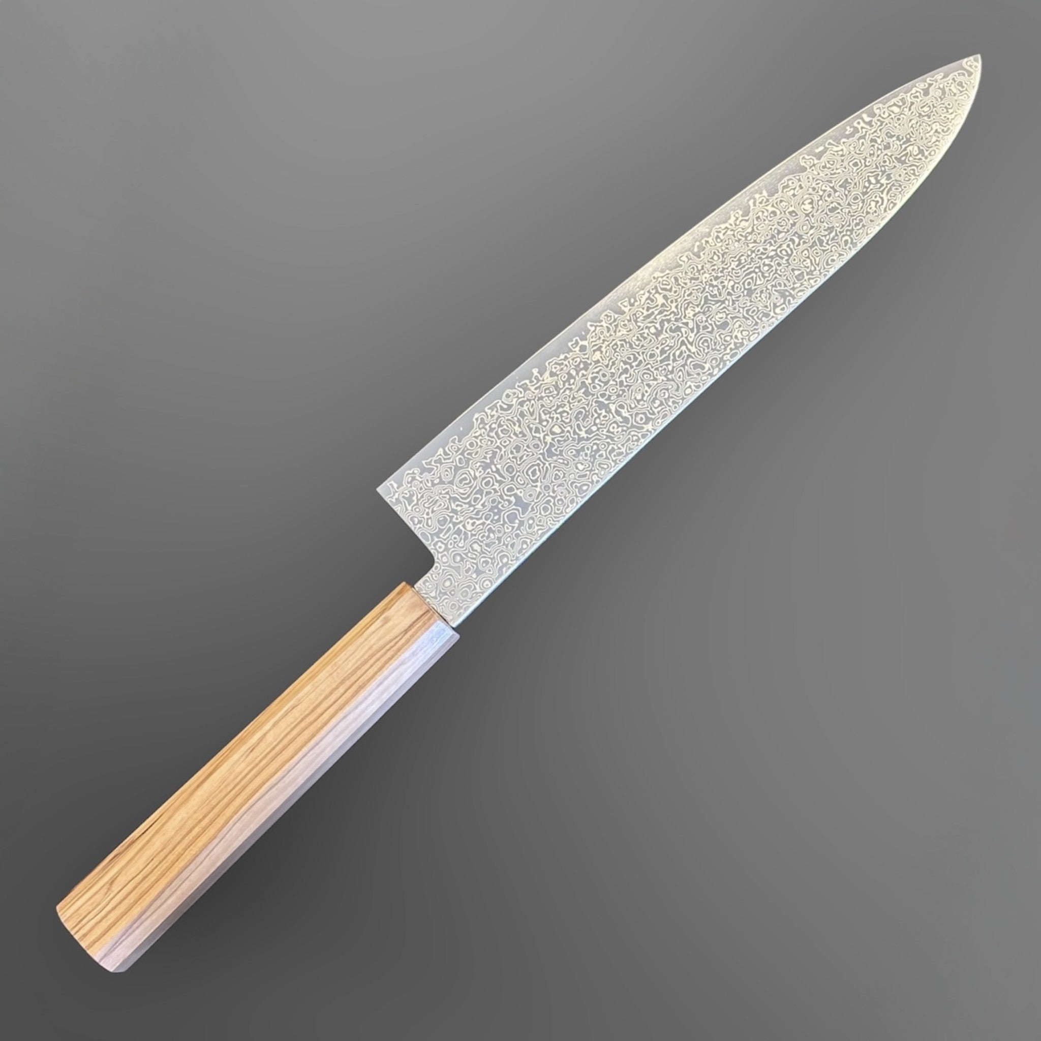 Hatsukokoro Saihyo SG2 Damascus Gyuto 210 mm with mono olive handle, close angled product view highlighting the flowing Damascus pattern and pointed gyuto profile.