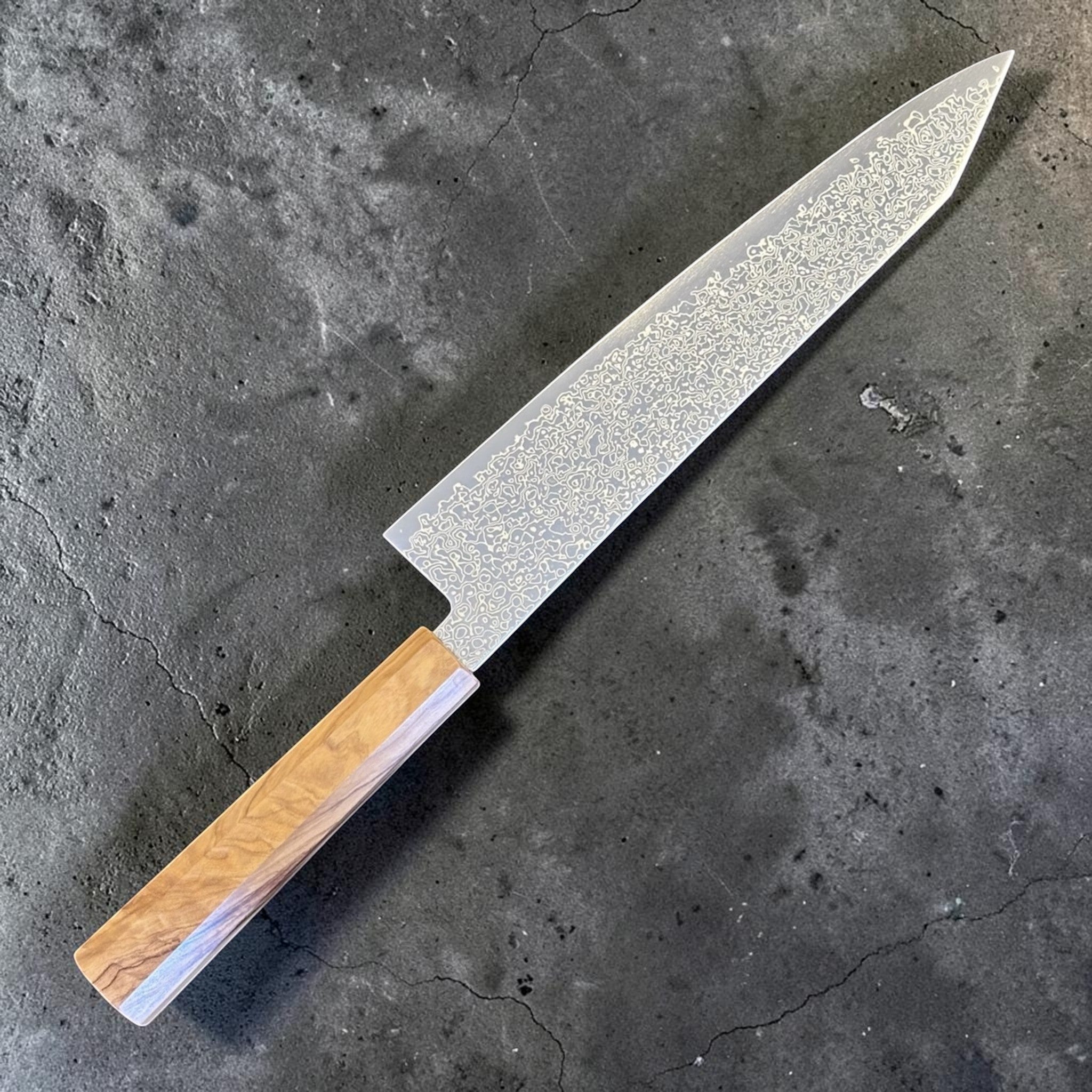 Hatsukokoro Saihyo SG2 Damascus Kiritsuke 240mm with Mono Olive Wood Handle, alternate angled full-length product view highlighting the Damascus pattern and pale olive wood handle.