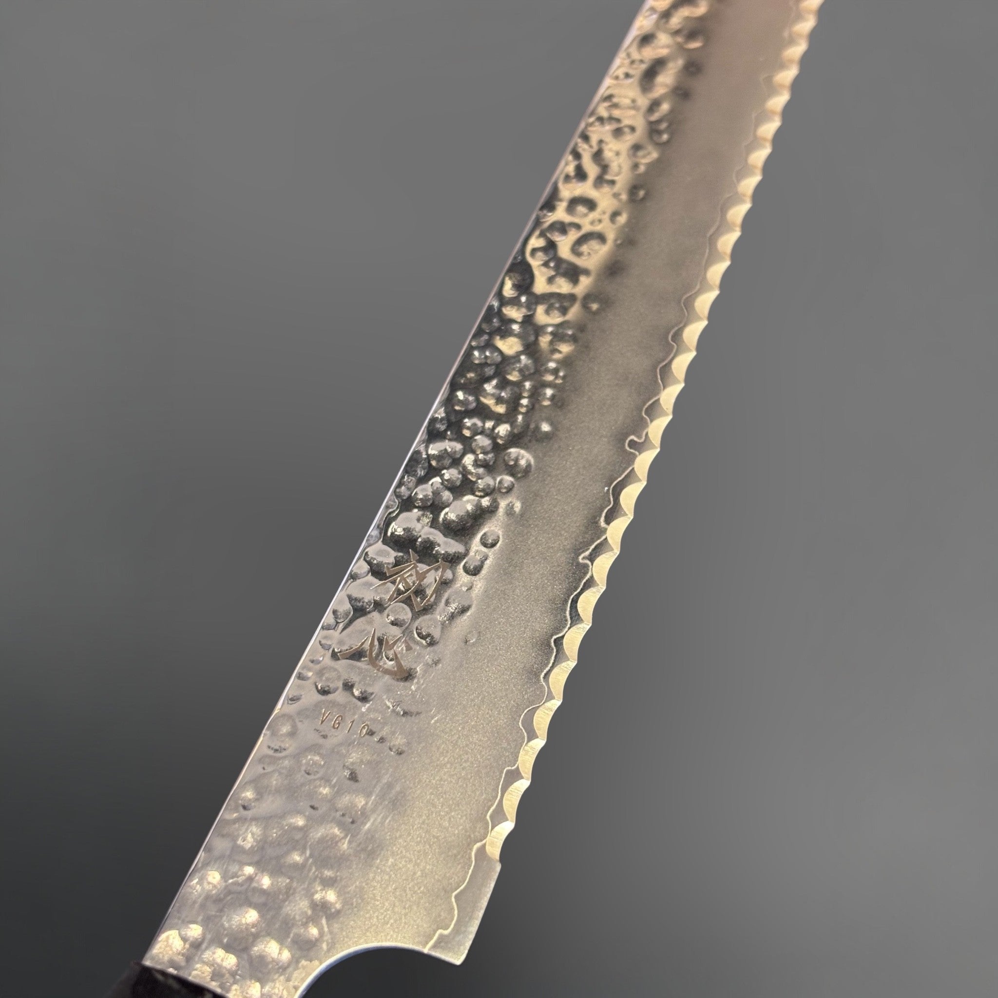 Hatsukokoro VG-10 Tsuchime Serrated Bread Knife 230 mm with burnt wood and black buffalo horn handle, close-up of hammered tsuchime blade face and serrated edge.