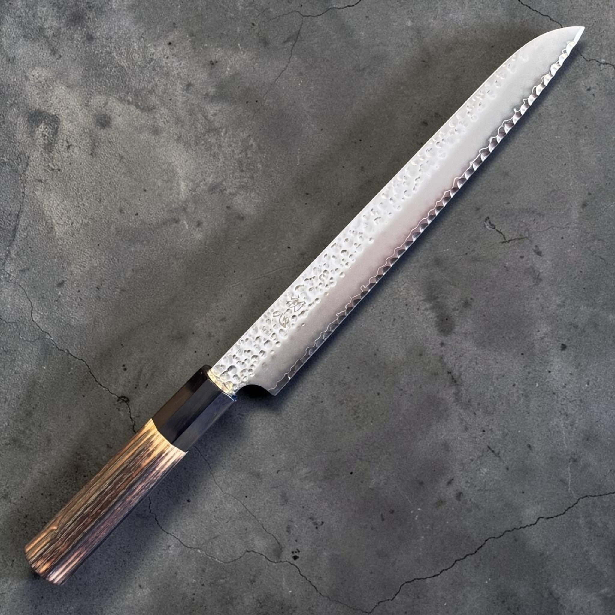 Hatsukokoro VG-10 Tsuchime Serrated Bread Knife 230 mm with burnt wood and black buffalo horn handle, angled product view highlighting the serrated edge and hammered blade finish.