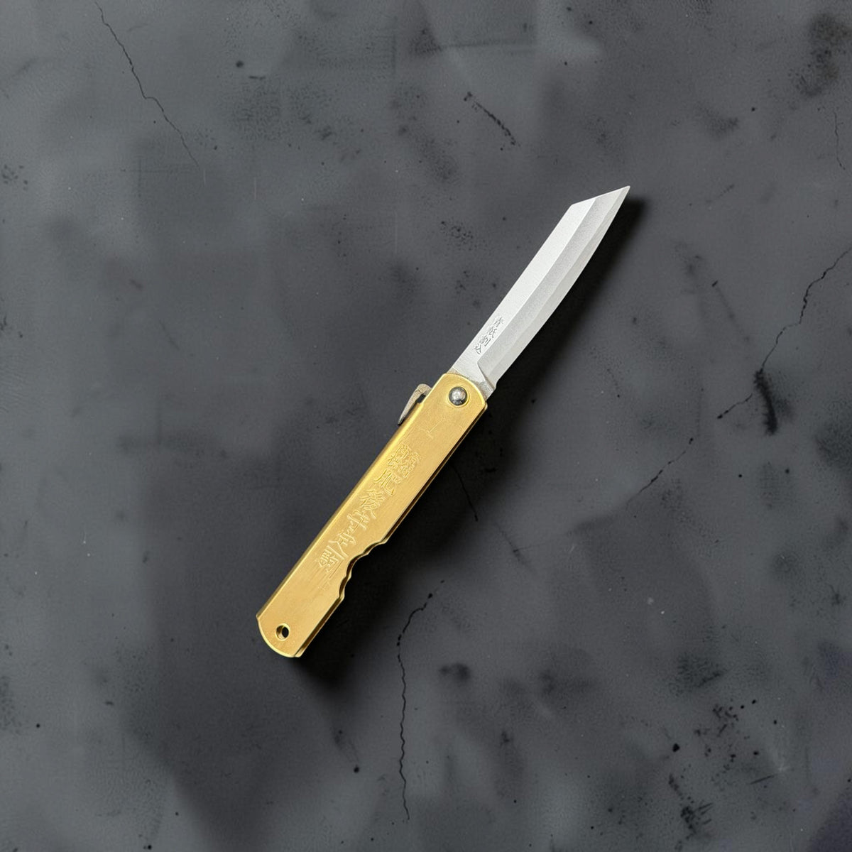 Higonokami Blue #2 medium folding knife open, showing the brass handle, maker stamps and polished blade on a dark grey background.