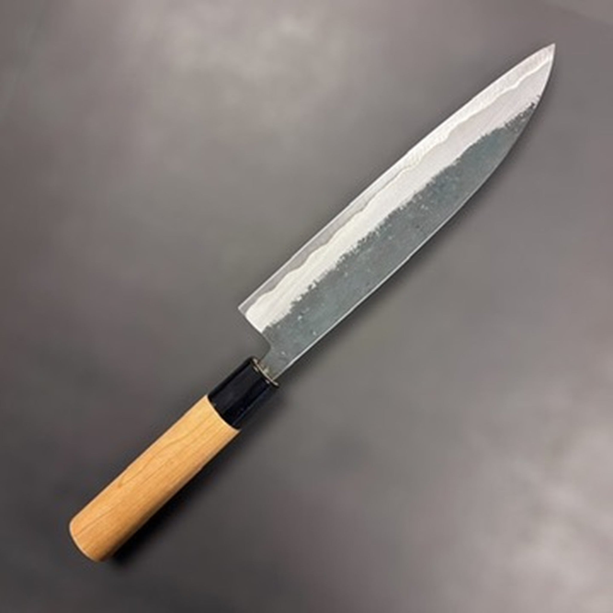 Hinokuni Aogami Super Kurouchi Gyuto 210 mm, opposite side three‑quarter view highlighting the core/cladding line.
