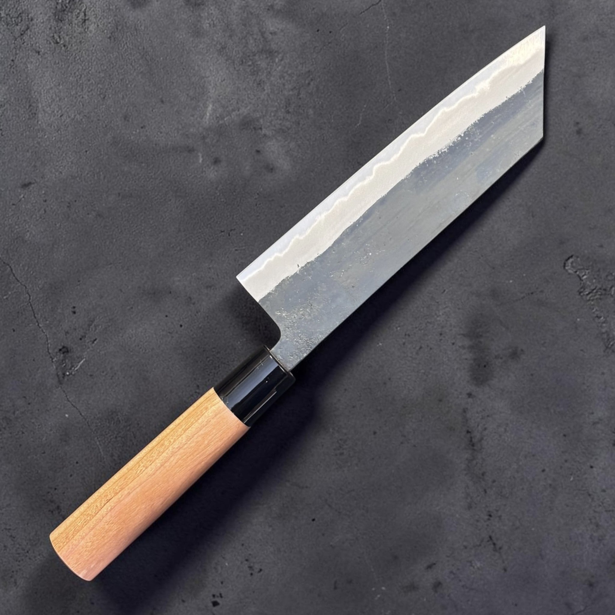 Hinokuni White #1 Kurouchi Bunka, angled full view showing the wide bevel and light wood handle with black ferrule.