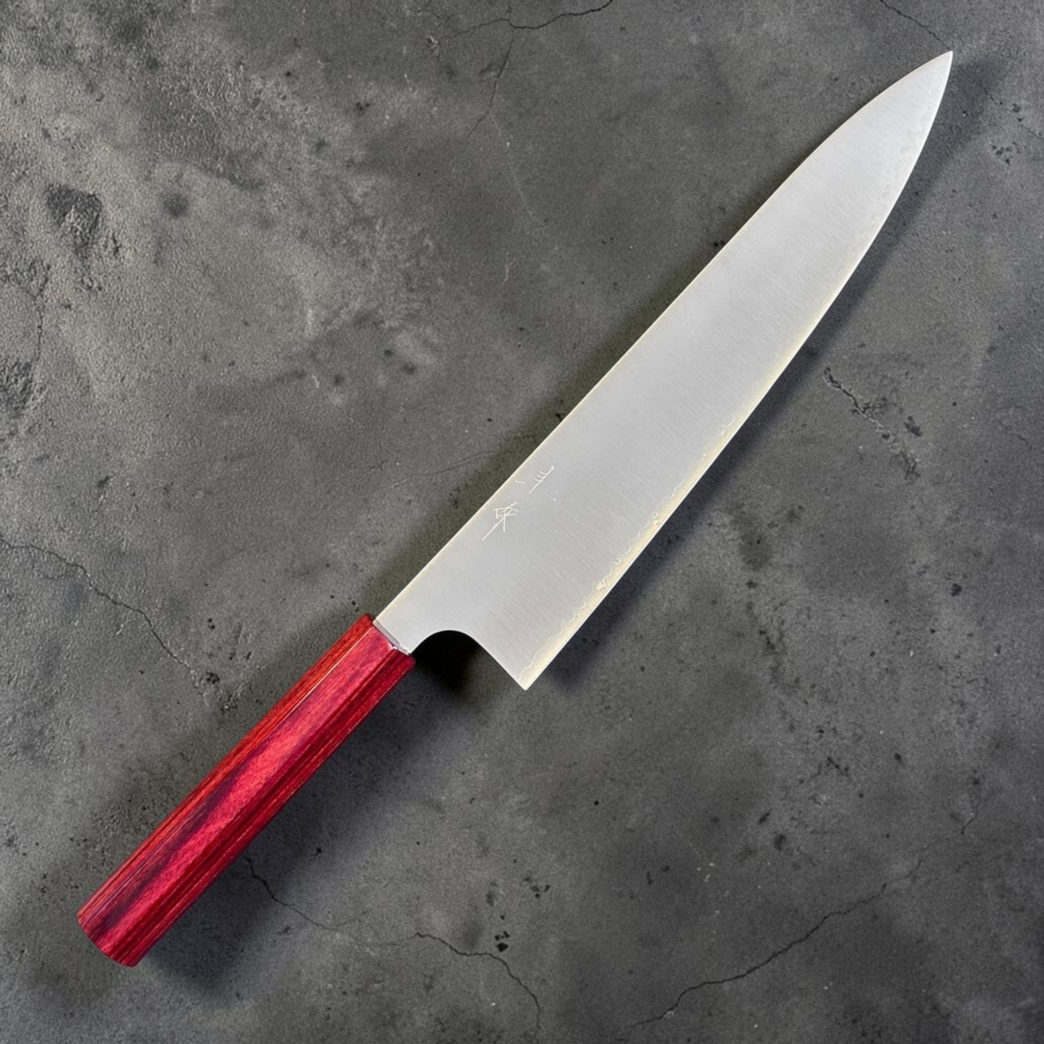 shi SG2 Gyuto 240 mm with red lacquer handle, angled front-side close-up highlighting the engraved kanji, polished satin blade, and fine tip geometry.