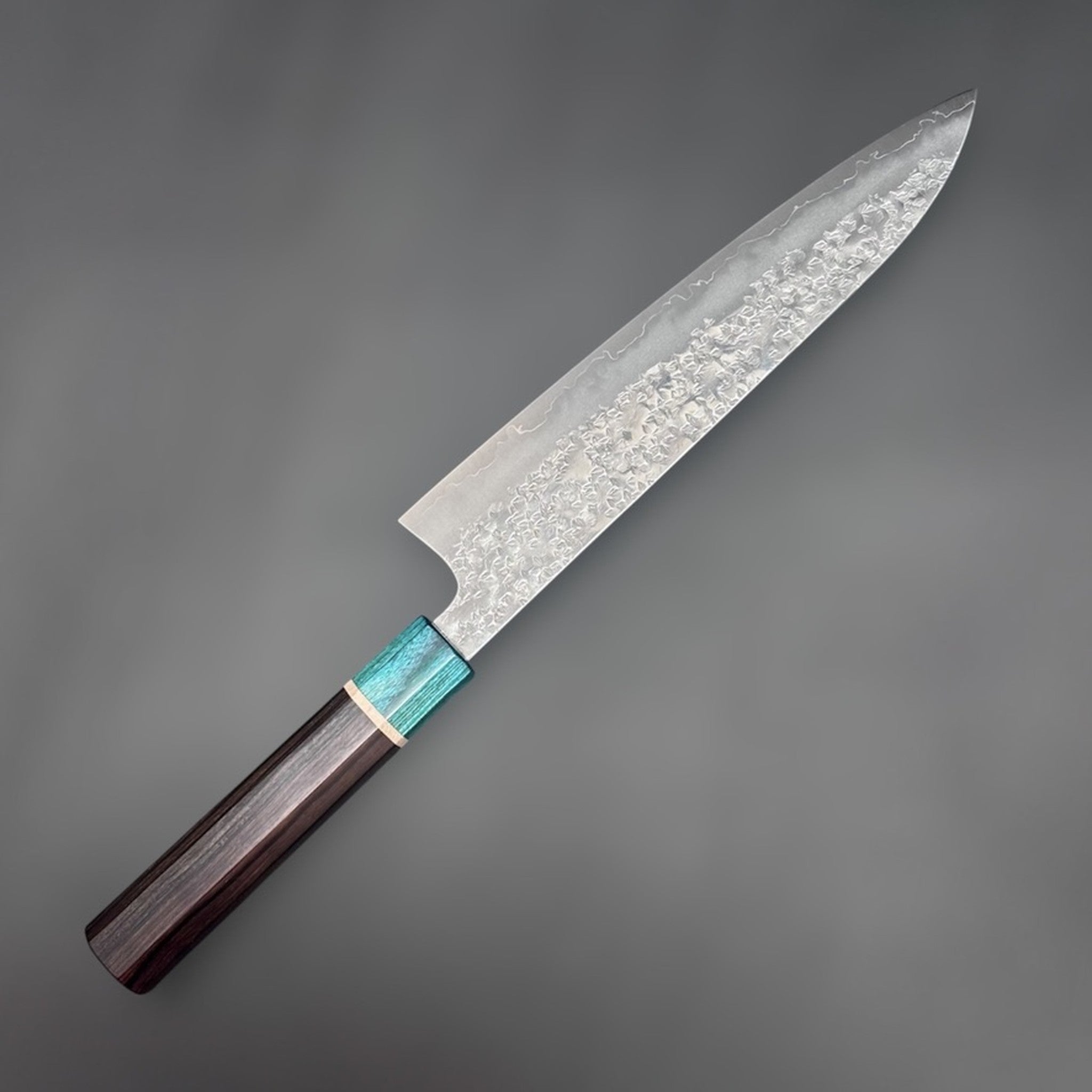 Makoto Kurosaki Samidorizuki SG-STRIX Gyuto 210 mm, angled blade detail highlighting the textured hammered finish and bright cladding line.