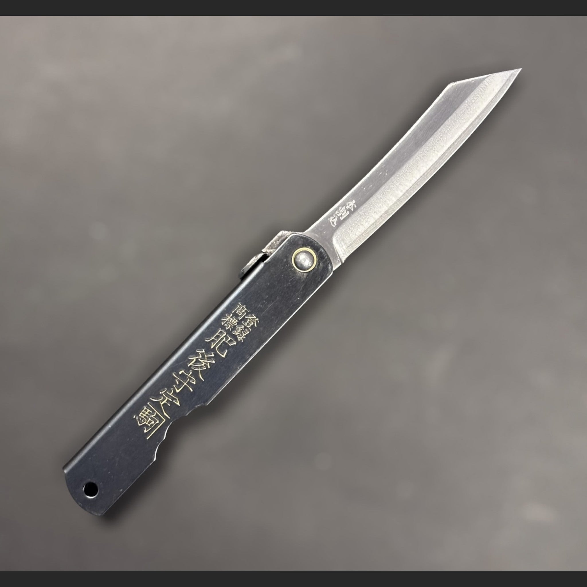 Nagao Higonokami SK carbon steel medium friction folder fully open, showing curved SK carbon blade and engraved black handle on neutral grey backdrop.