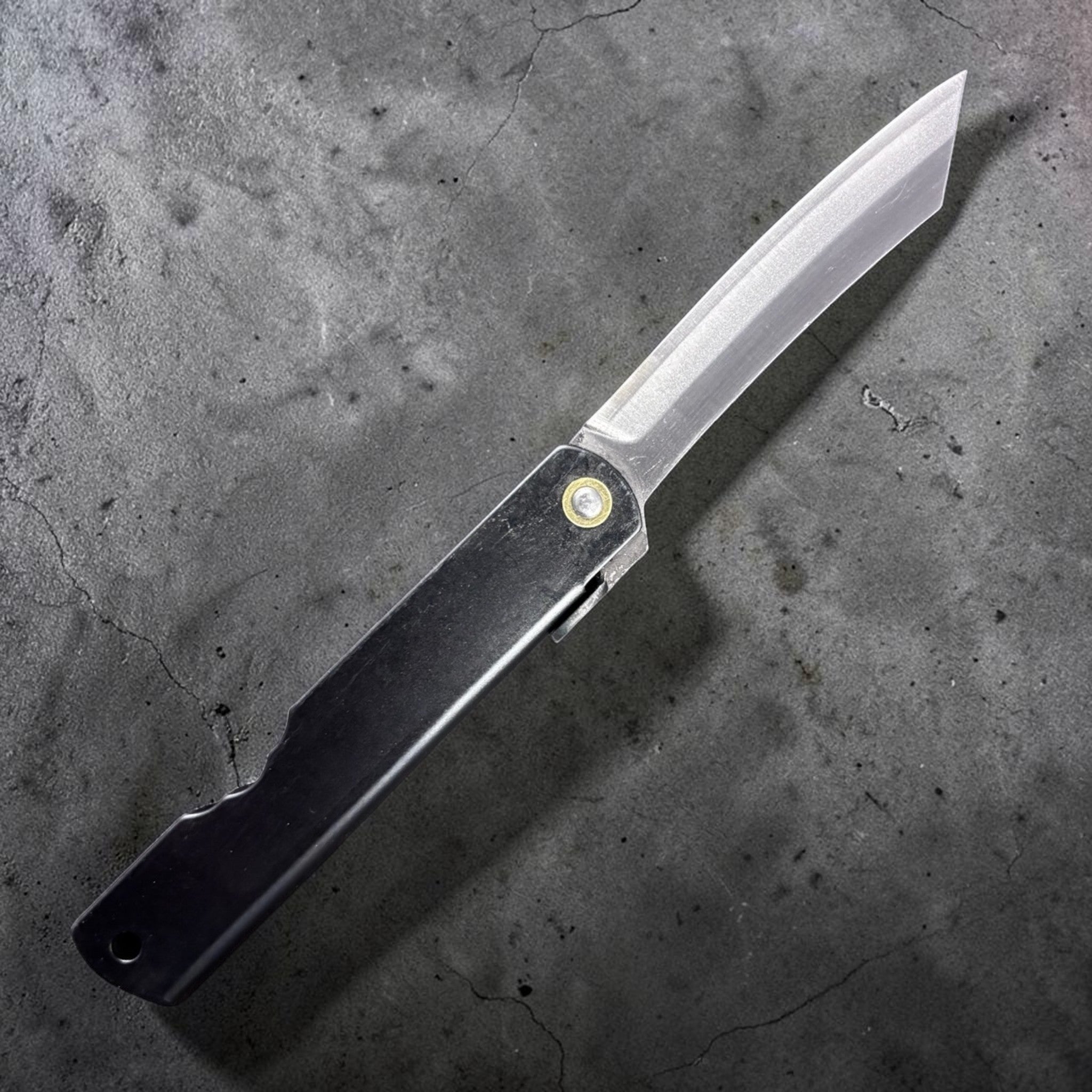 Reverse side of Nagao Higonokami SK carbon steel medium friction folder with plain black handle and SK carbon blade, studio-lit on dark background.